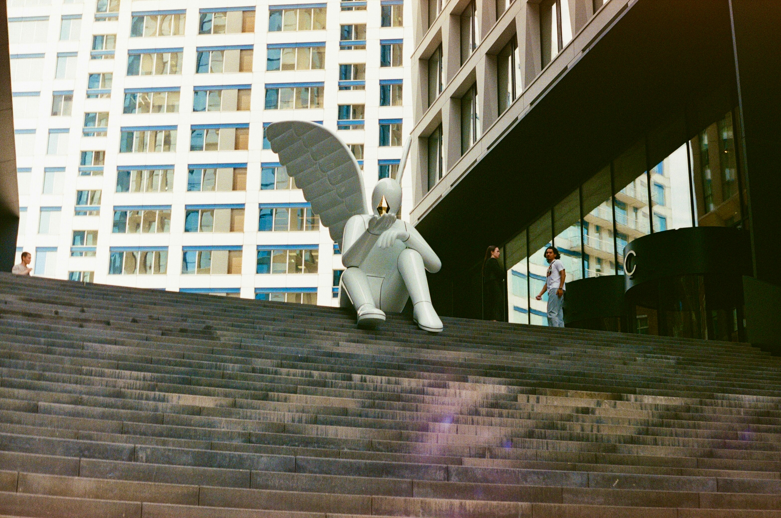 A white winged figure sits on stone steps.