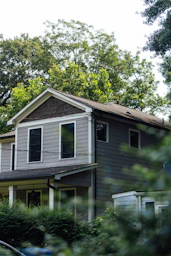 A gray two-story house surrounded by green trees