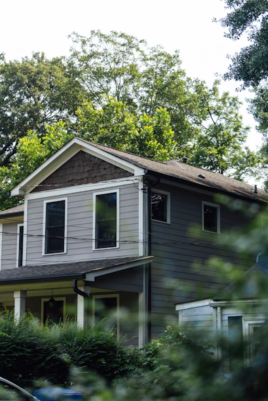 A gray two-story house surrounded by green trees
