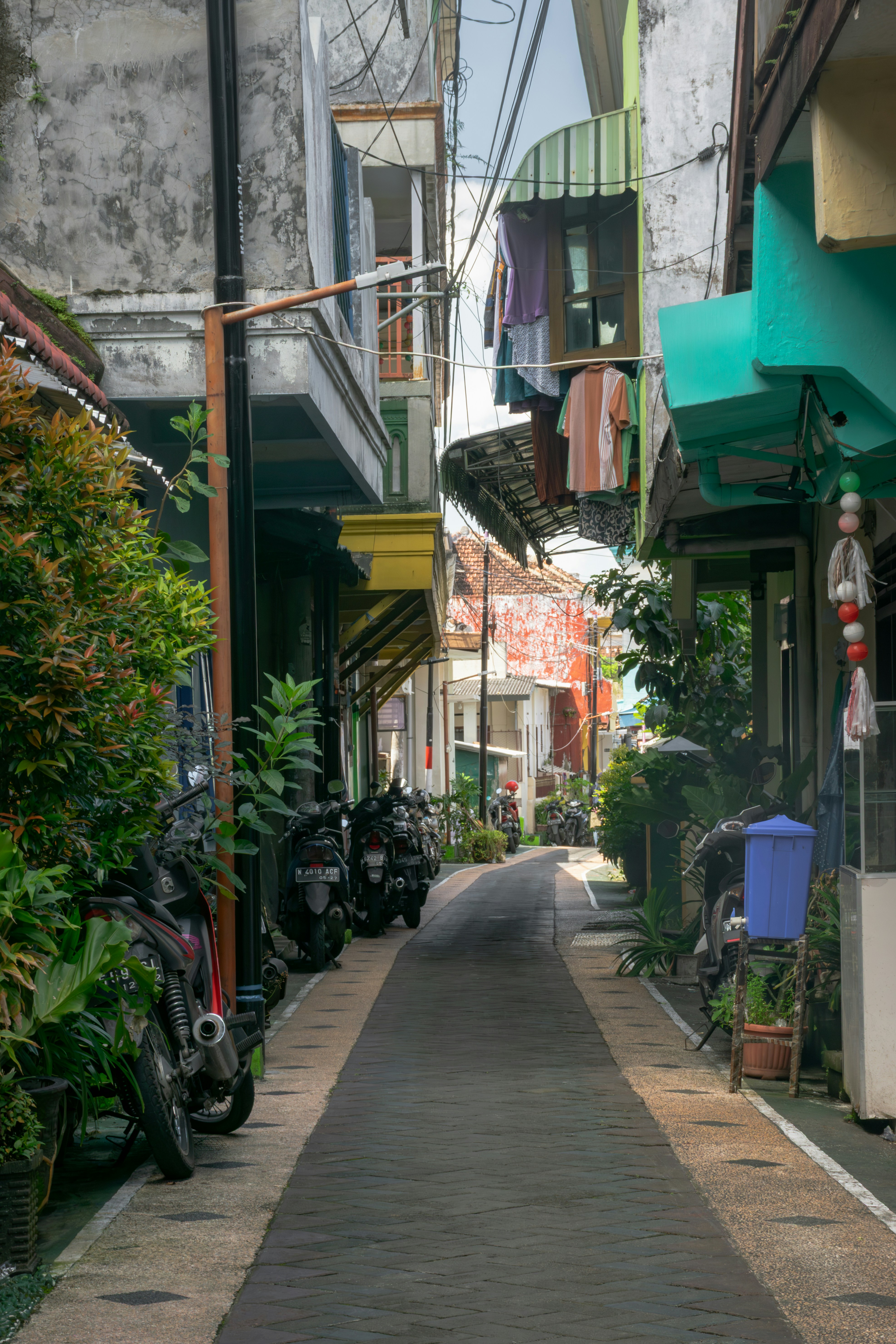 A narrow alleyway with buildings, parked motorcycles, and hanging laundry.