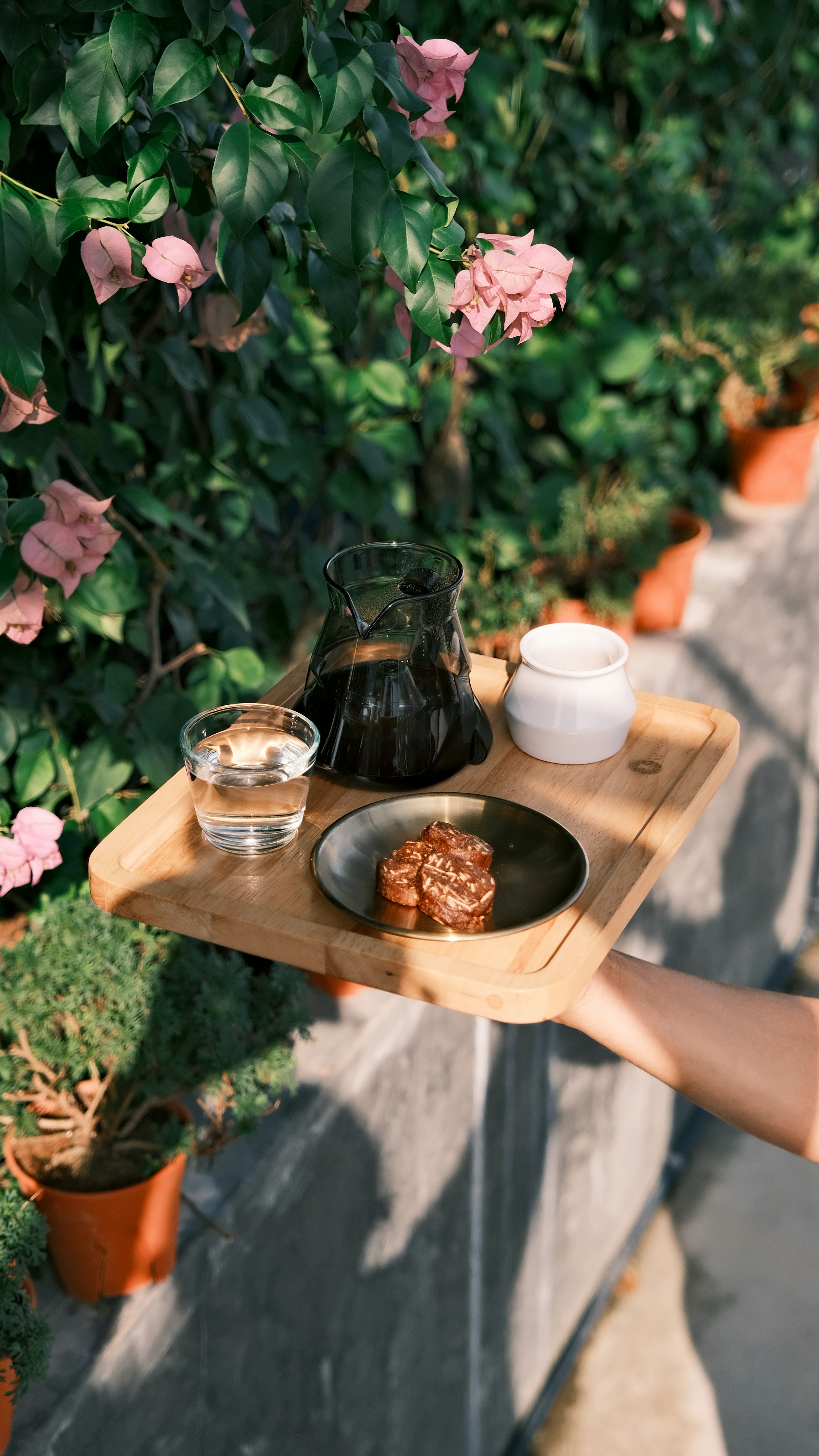 コーヒー、水、デザート、花を載せたトレイを手持ちで