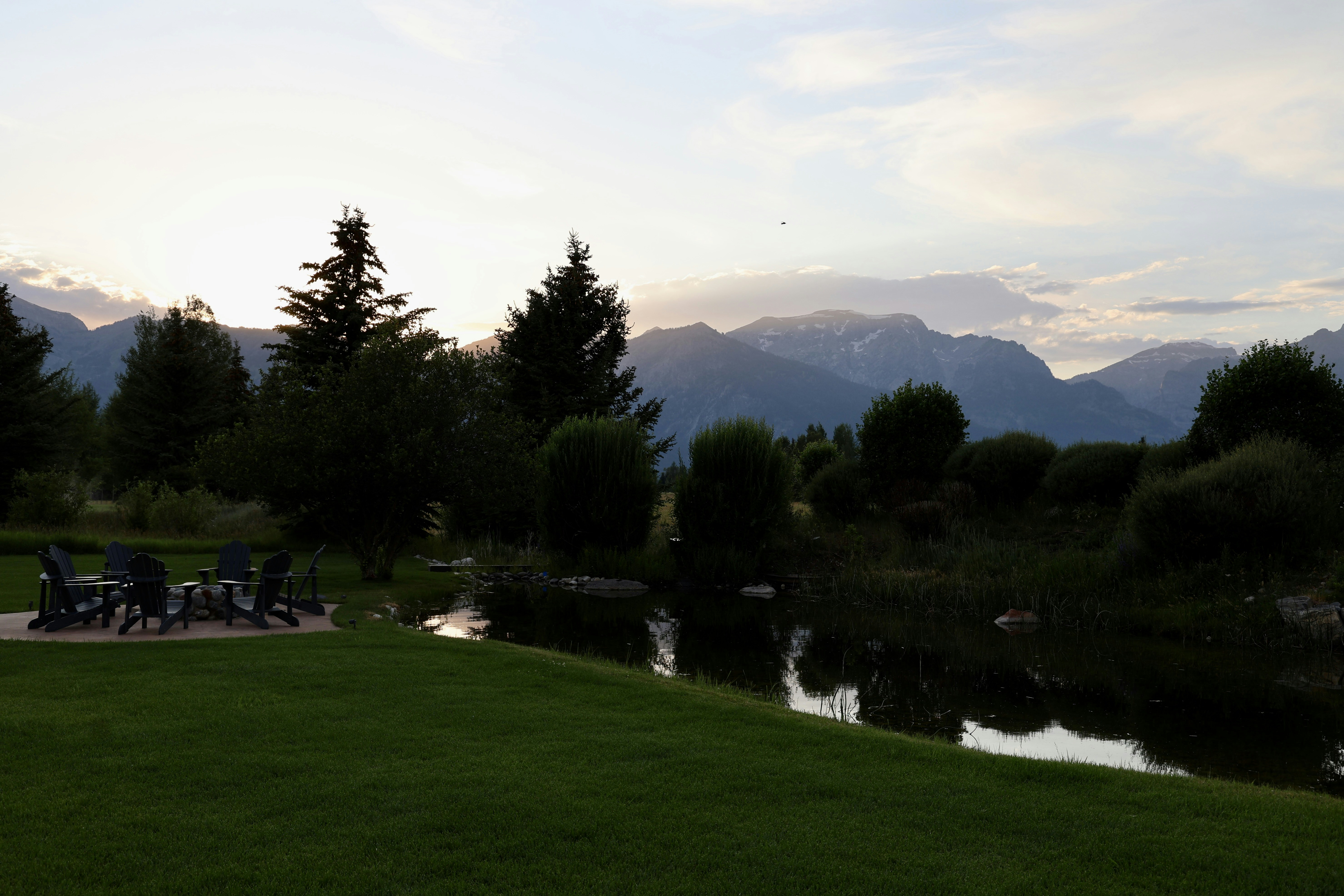 Mountains at sunset behind a pond and outdoor seating.