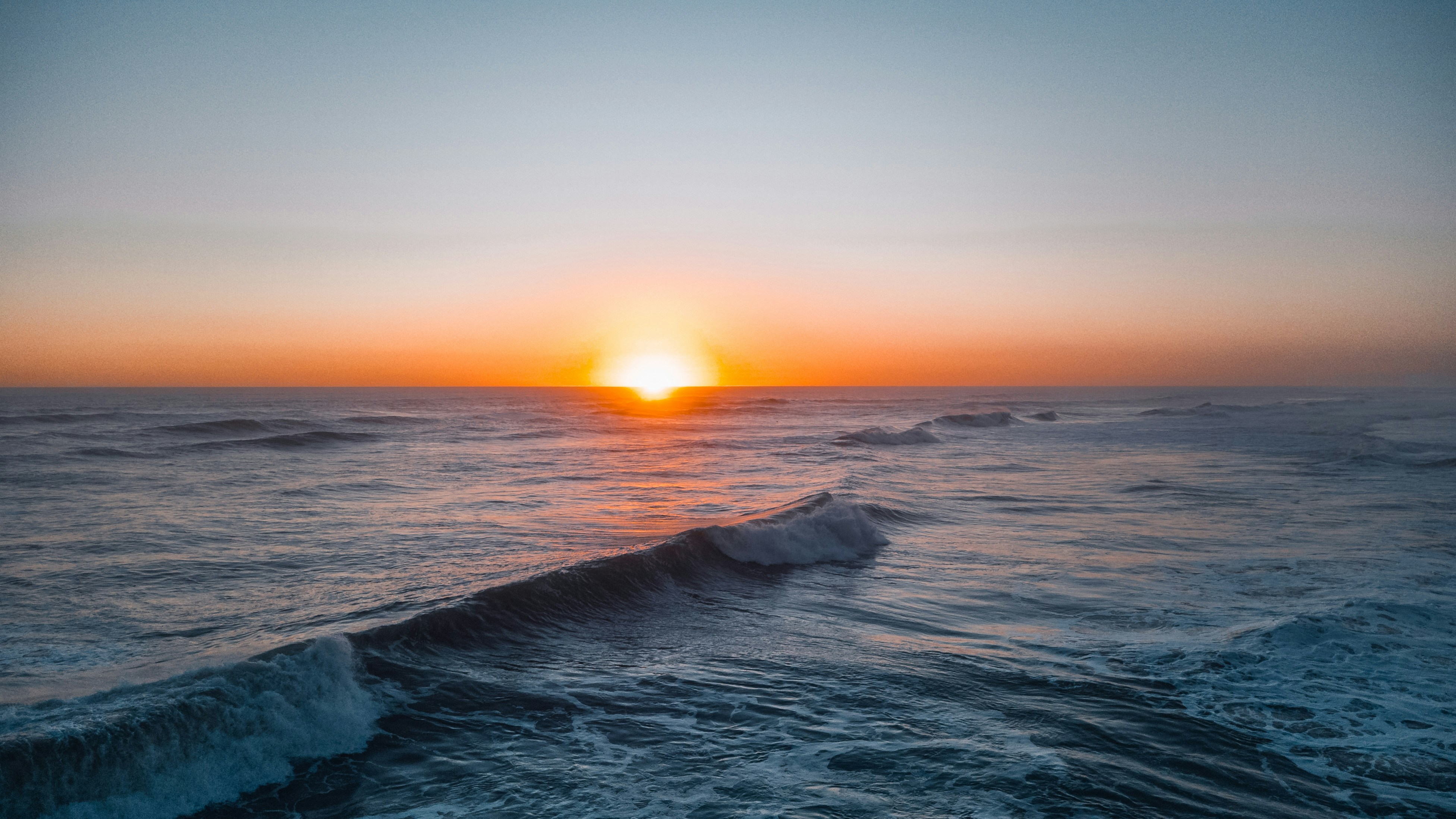 Golden sun setting over a dark, wavy ocean at dusk