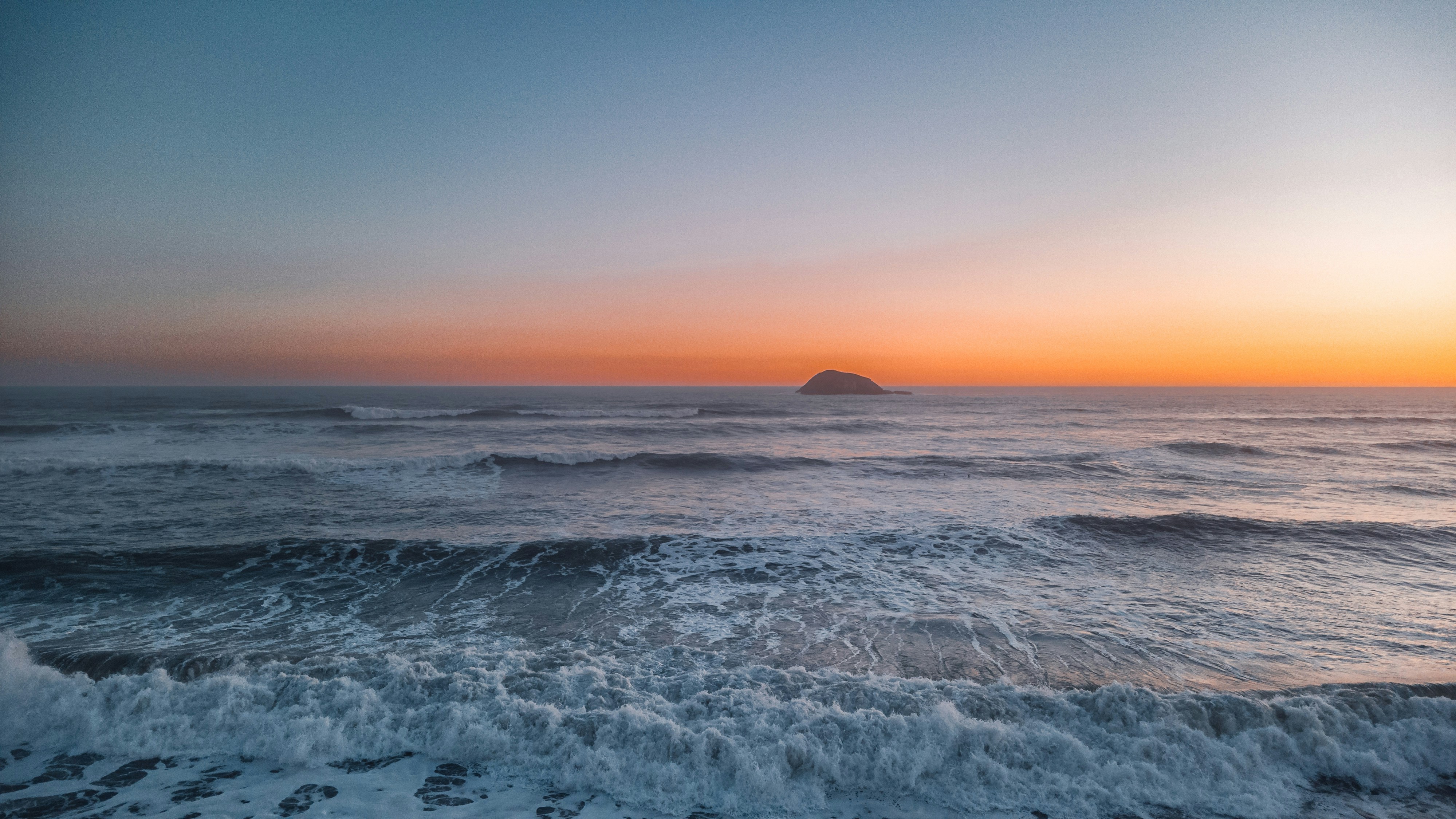 Ocean waves crashing at sunset with a distant island