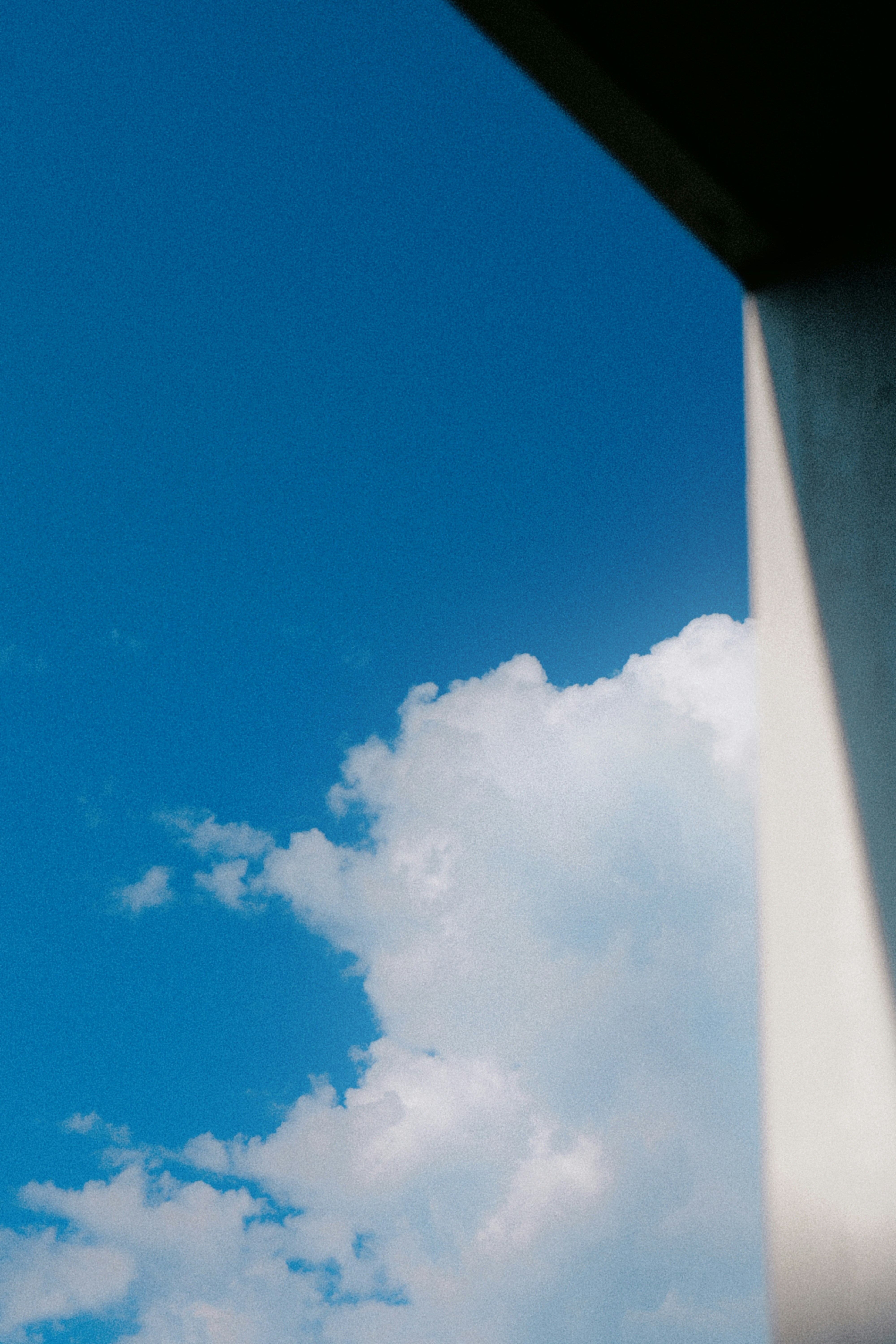 Blue sky with white clouds framed by a building edge