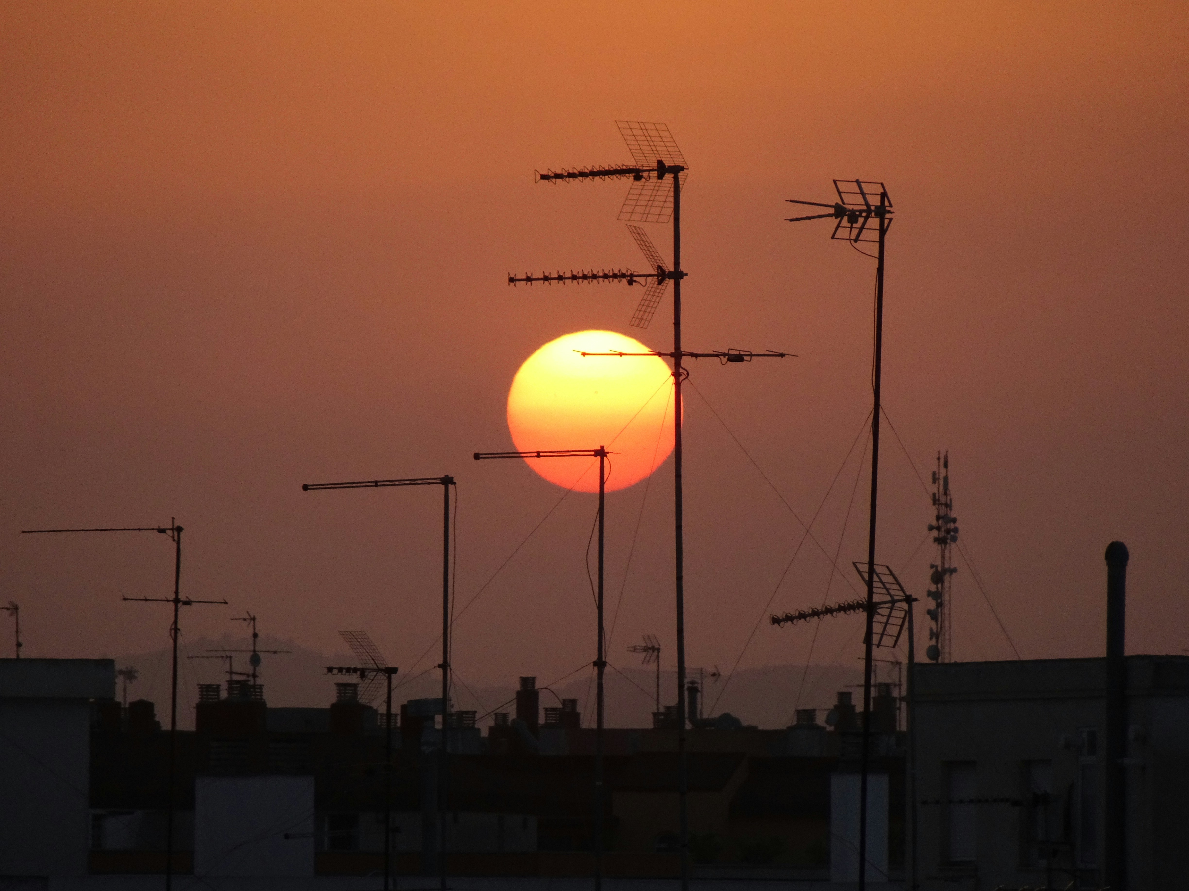 Un grande sole arancione tramonta dietro i tetti e le antenne delle città.
