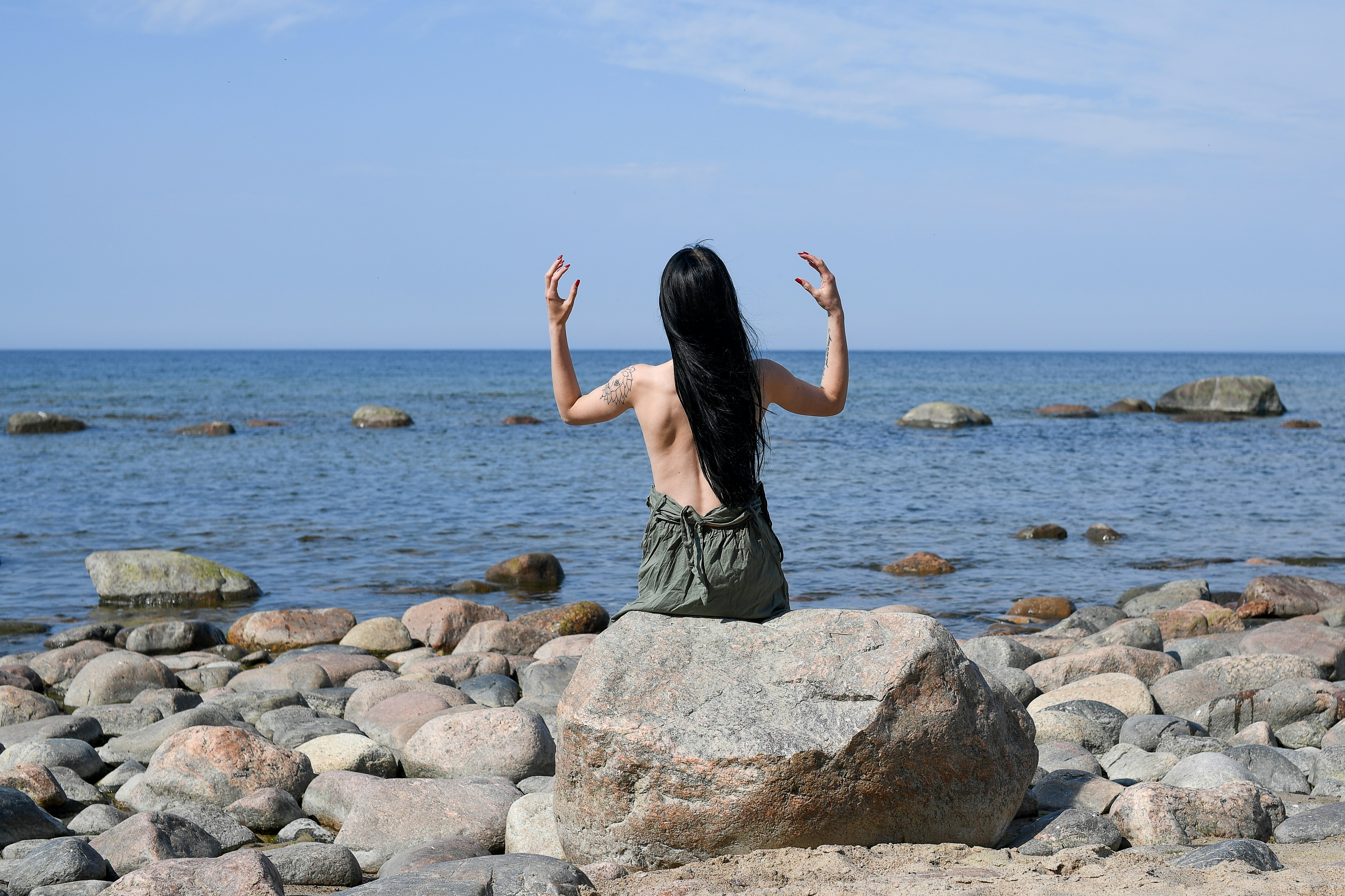 Mujer con los brazos levantados se sienta en una roca junto al mar