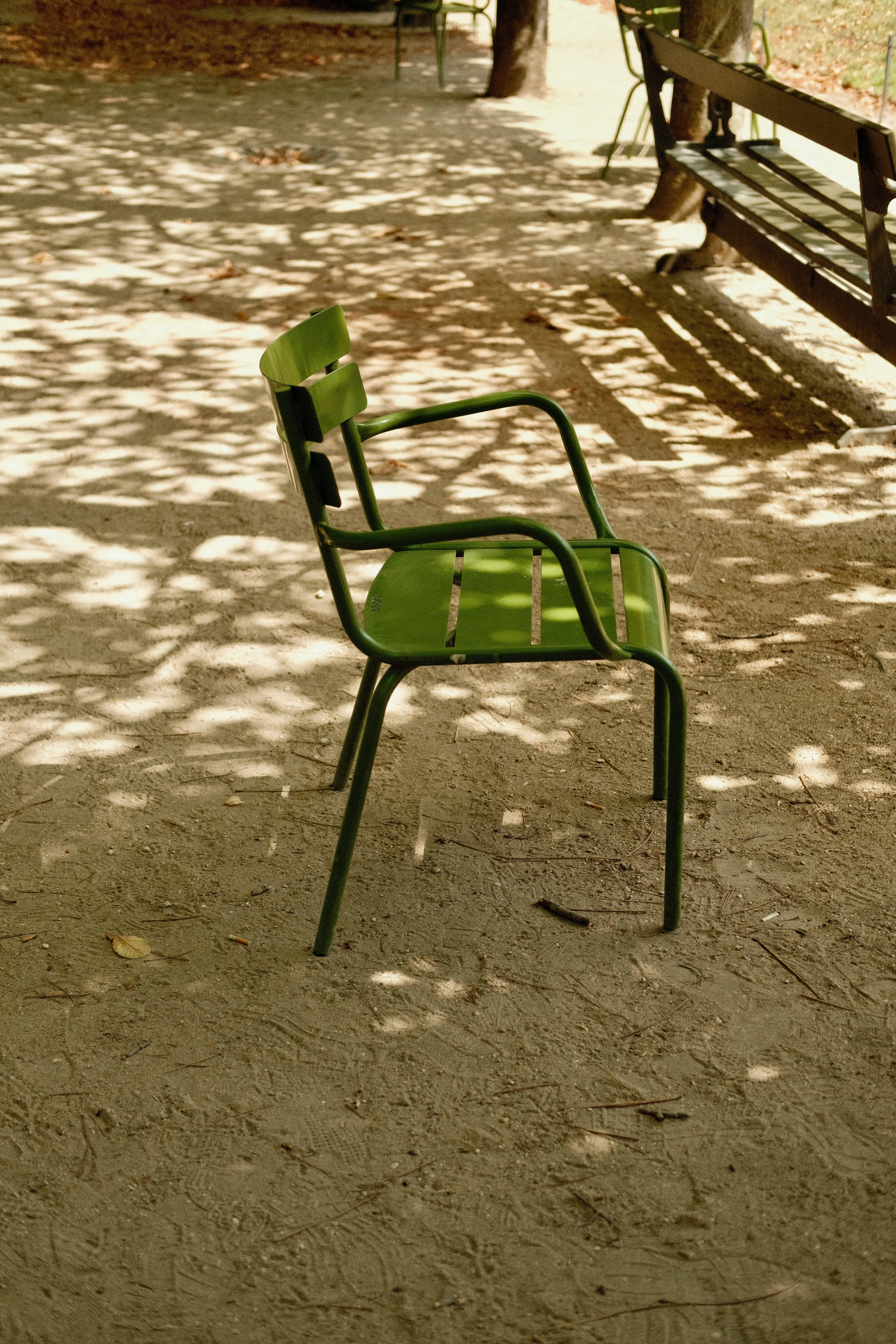 Green chair in a park with dappled sunlight and shadows