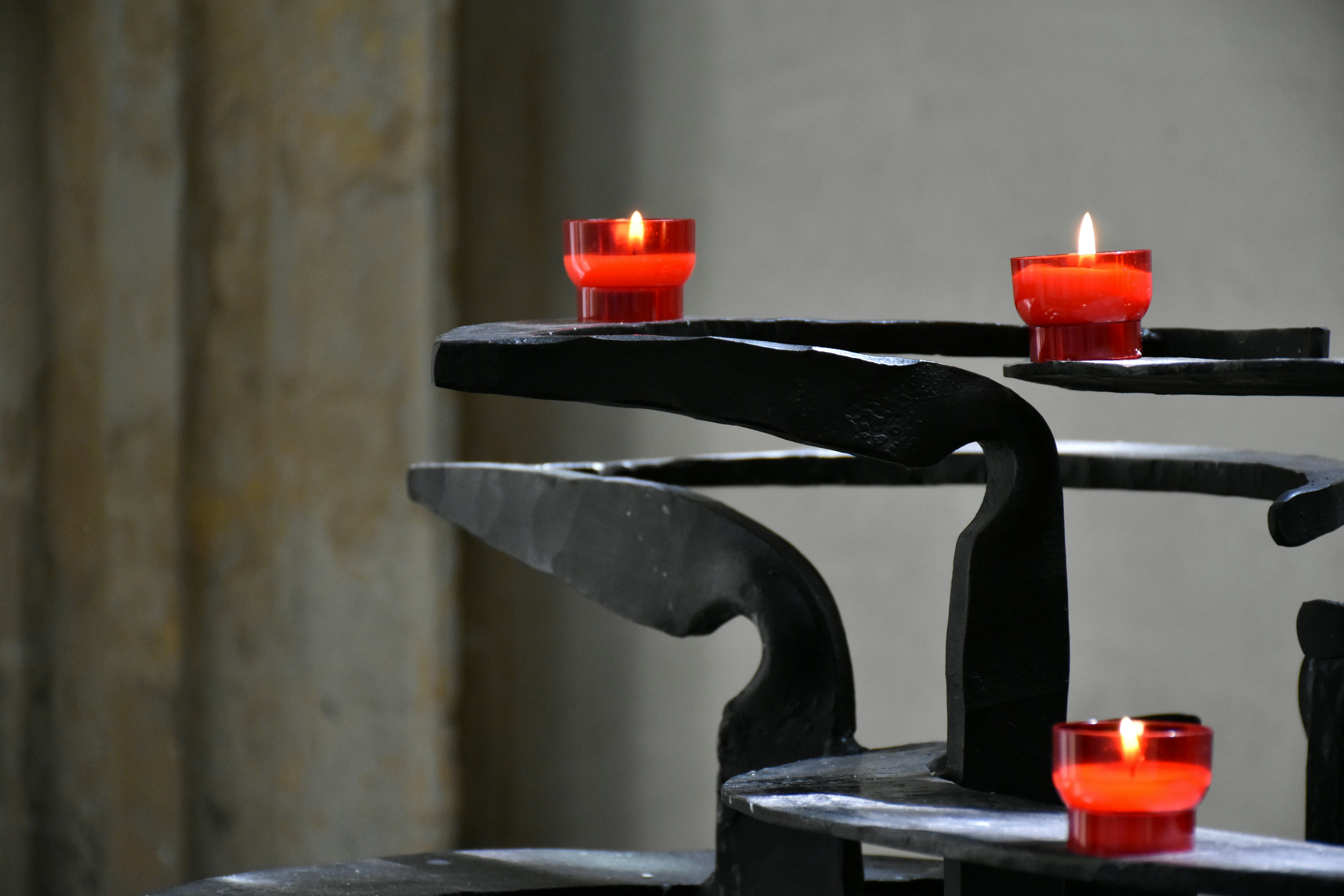 Three red votive candles burning on a dark metal stand.