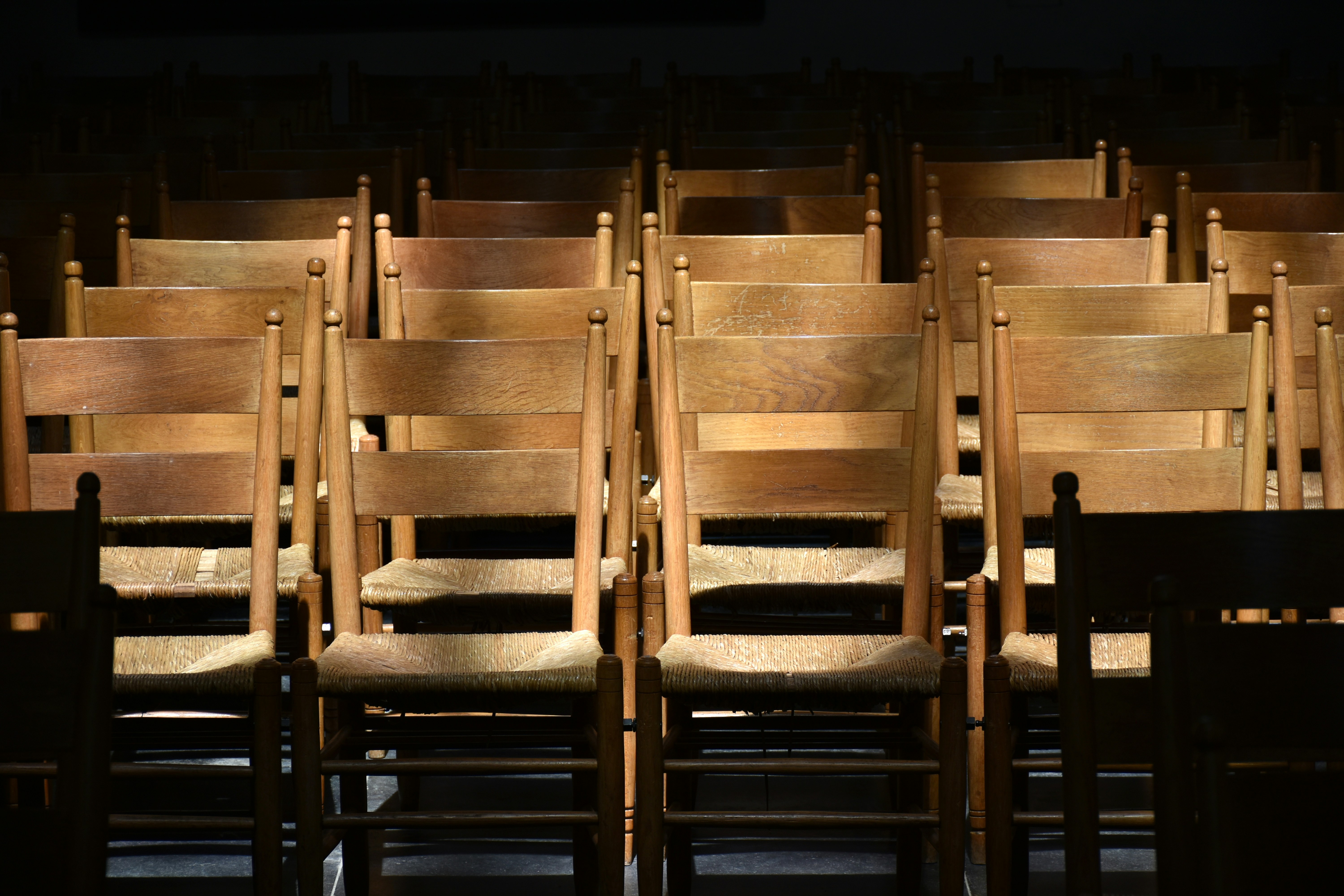 Rows of empty wooden chairs in a dimly lit room.