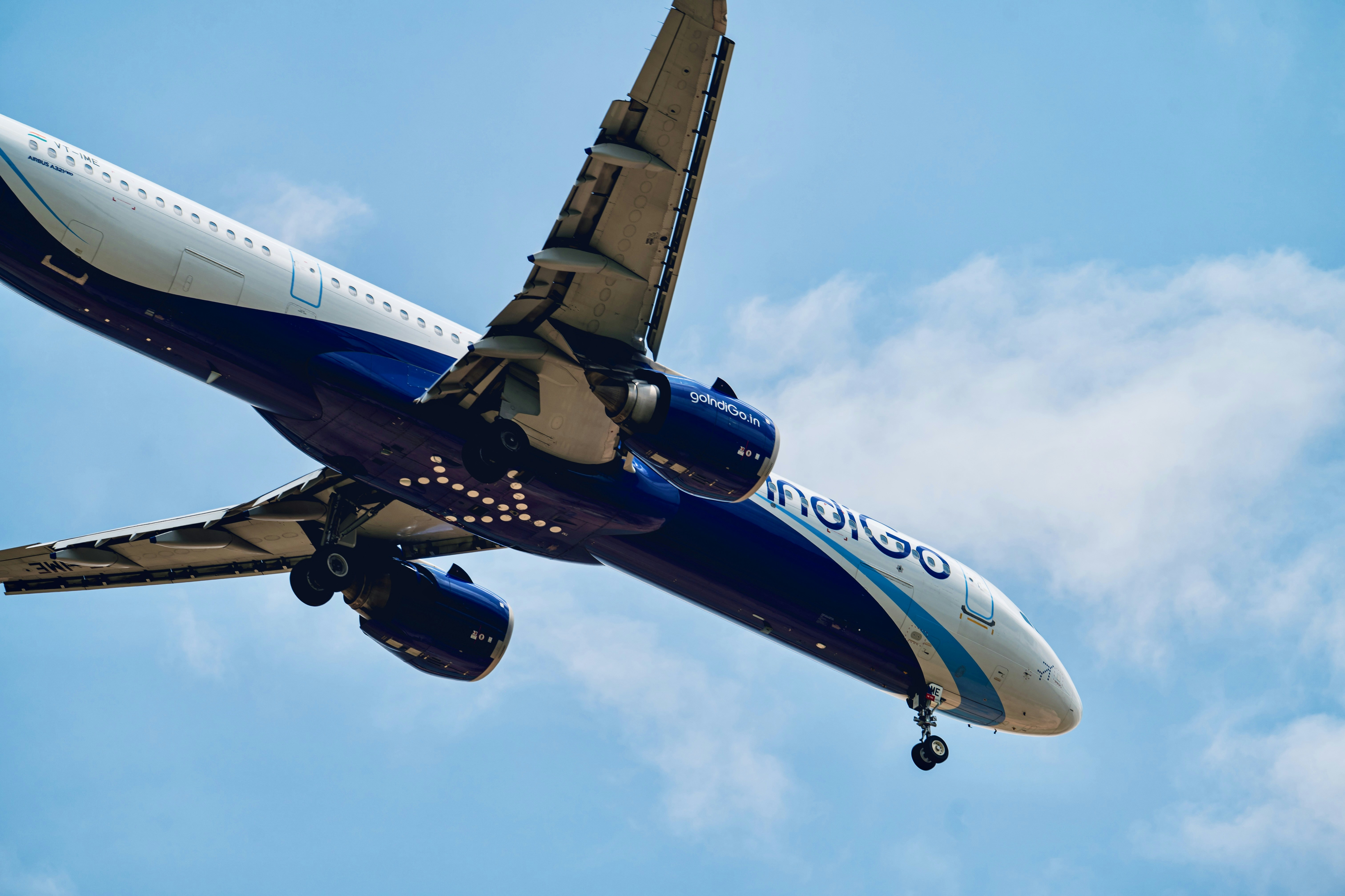 Indigo airplane with landing gear down against a blue sky.