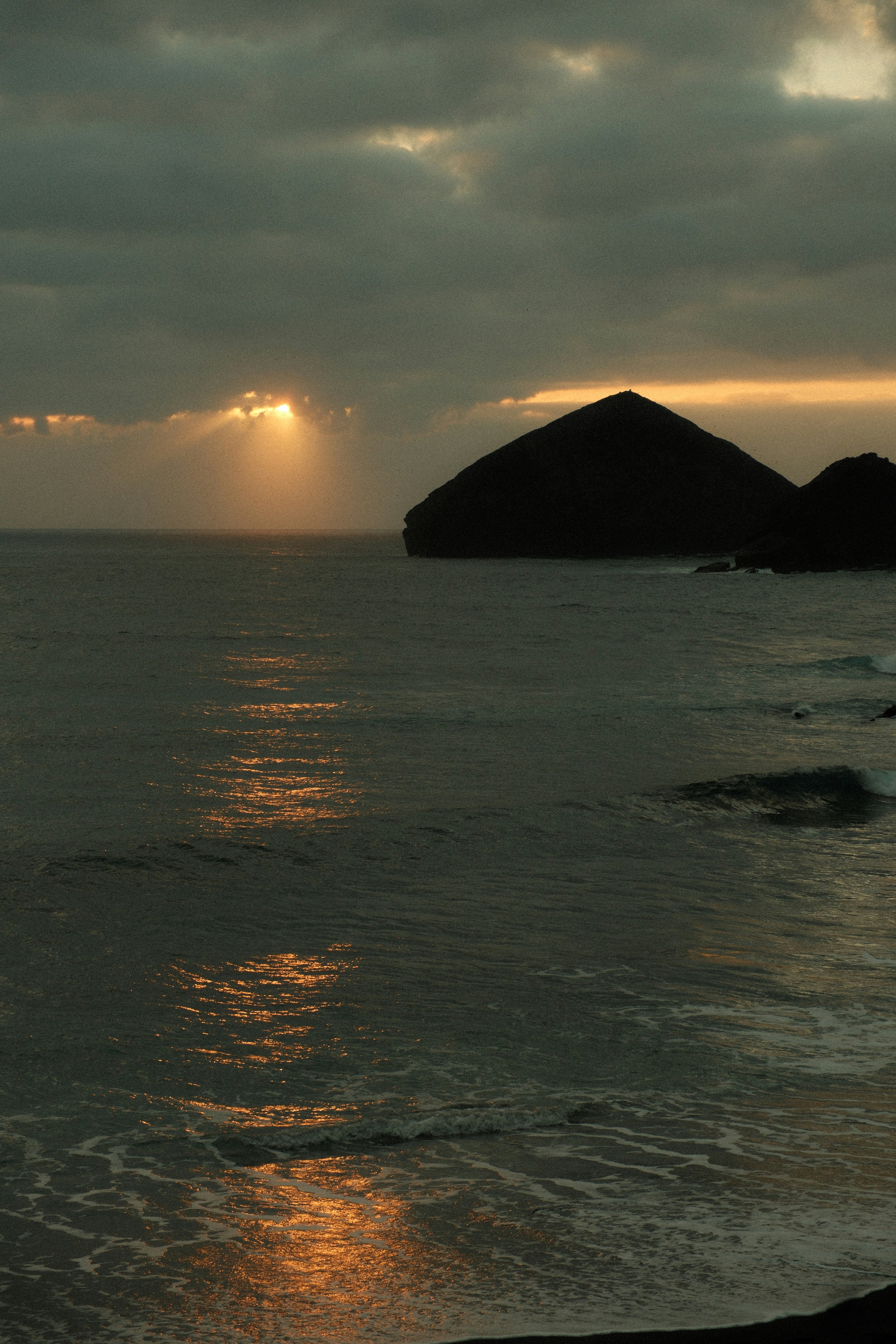 Golden sun rays reflect on ocean near a dark island