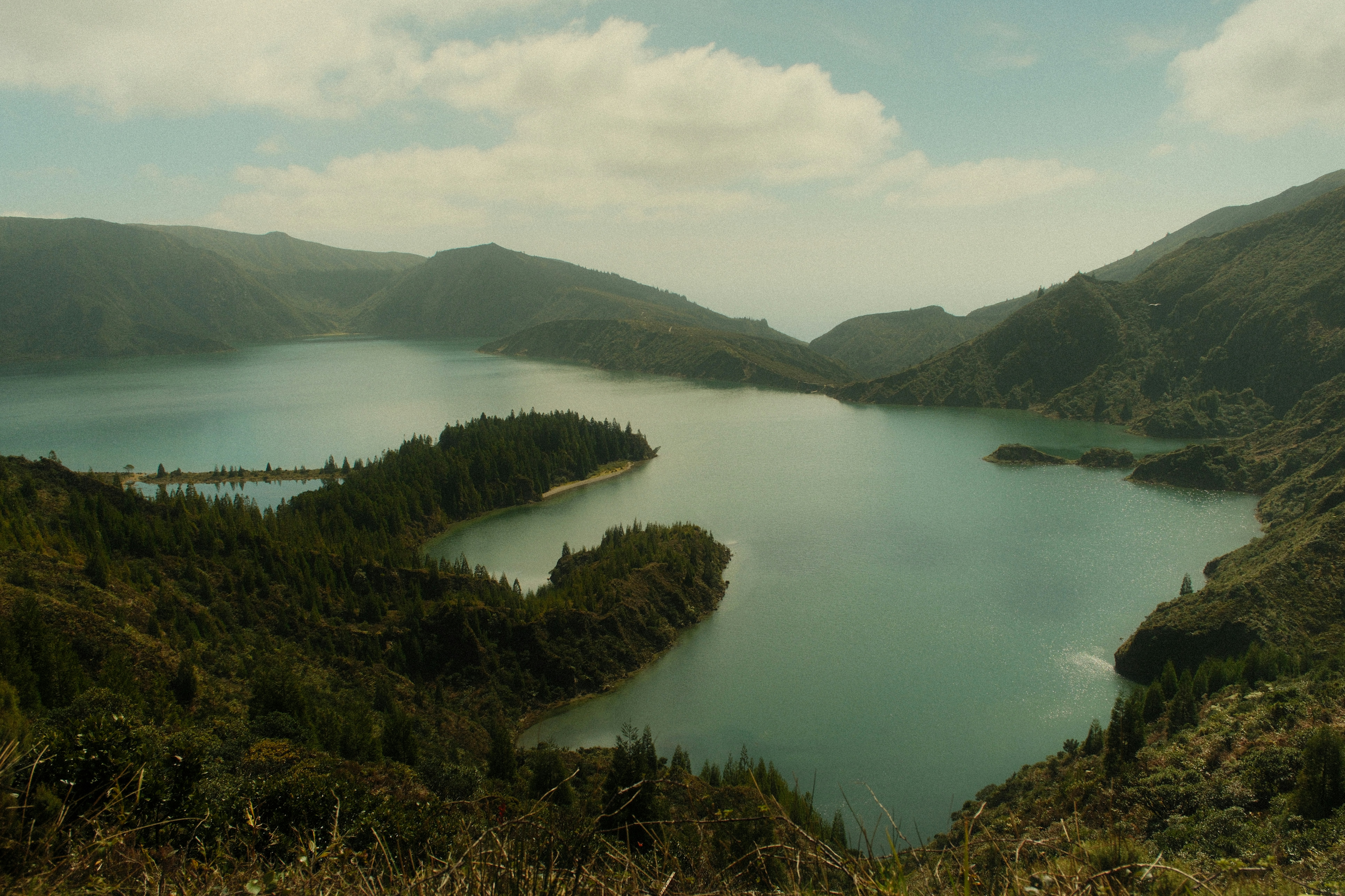 Serene lake surrounded by lush green hills under cloudy sky