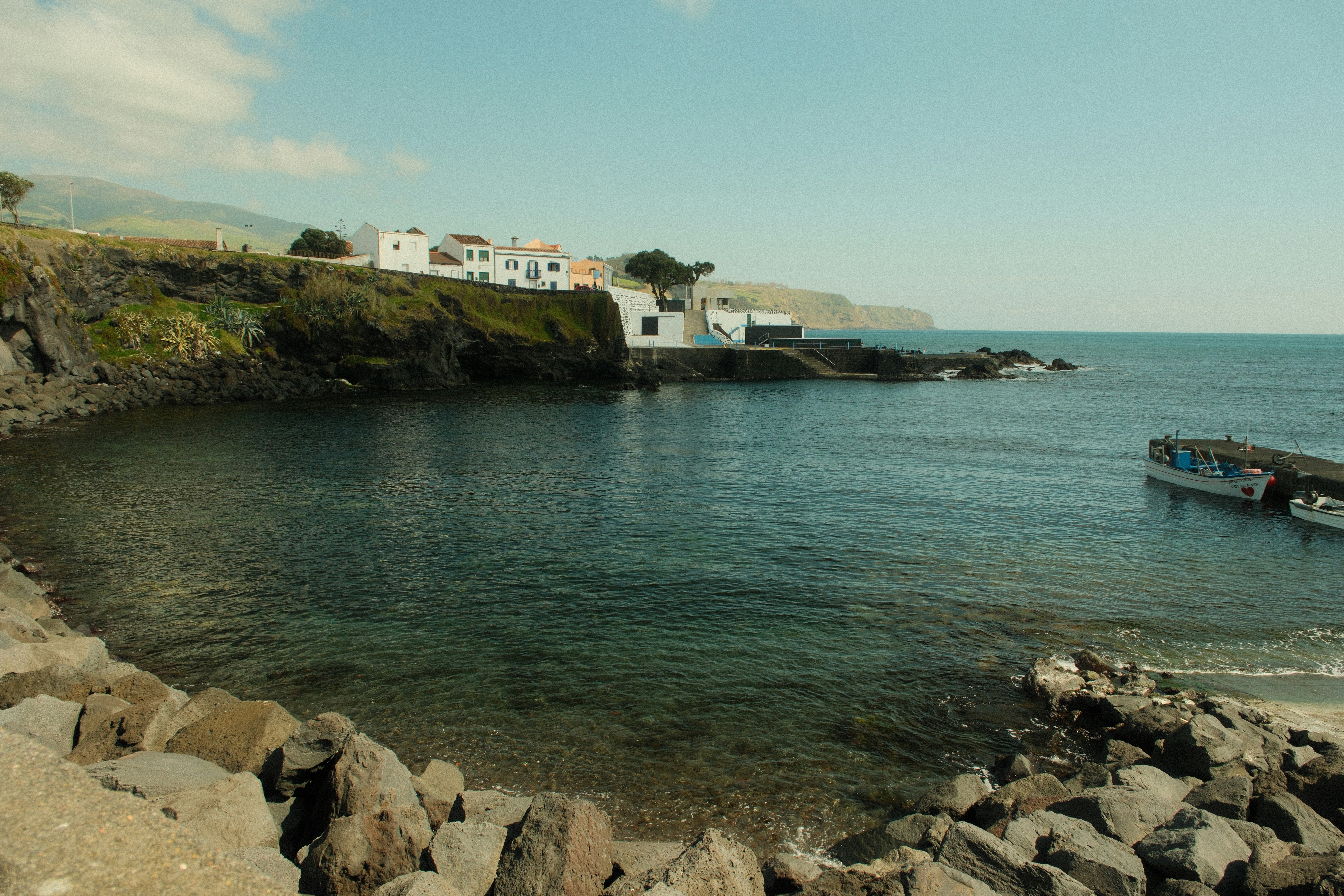 White buildings overlook a calm bay with a rocky shore