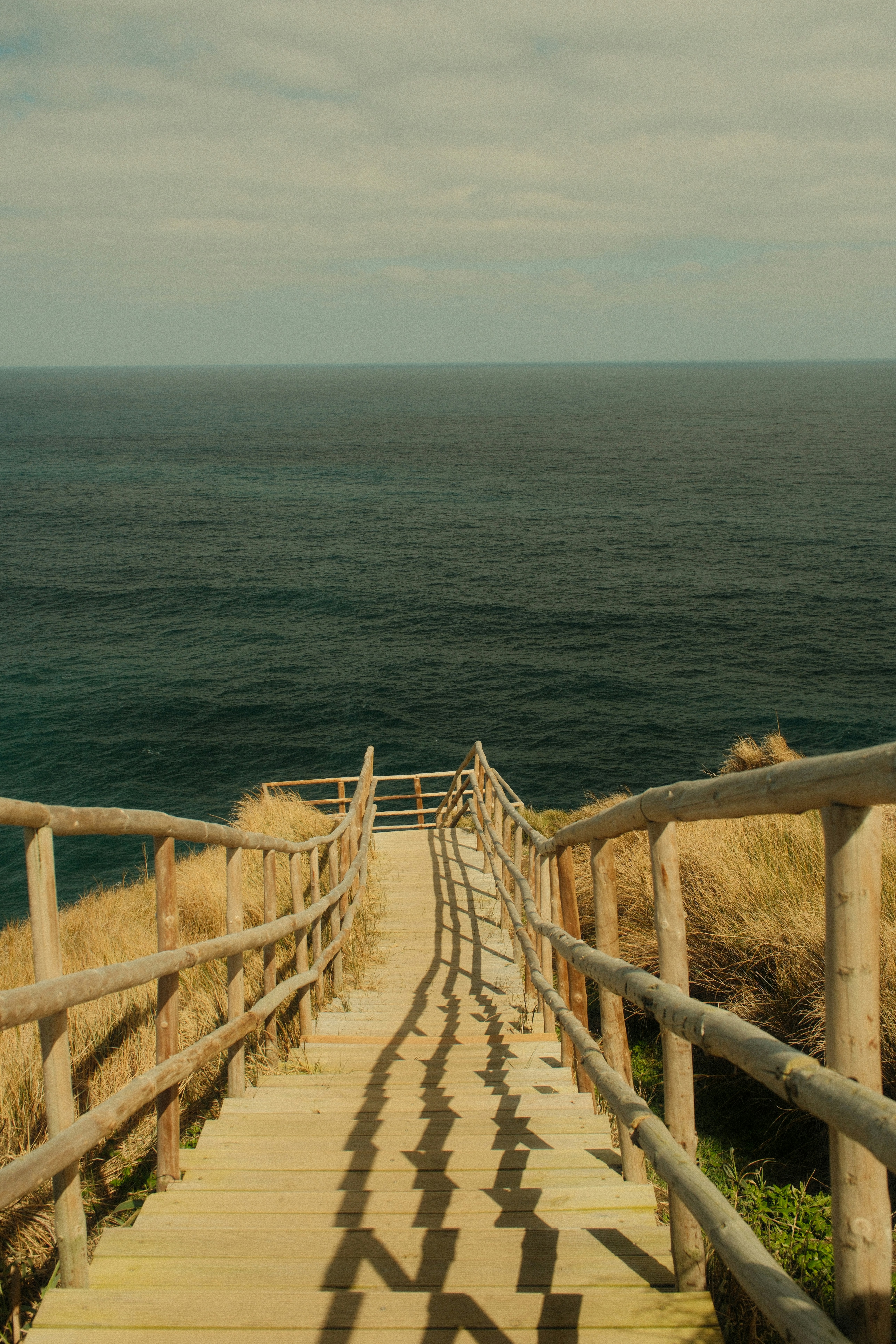Wooden stairs lead to the ocean under a cloudy sky