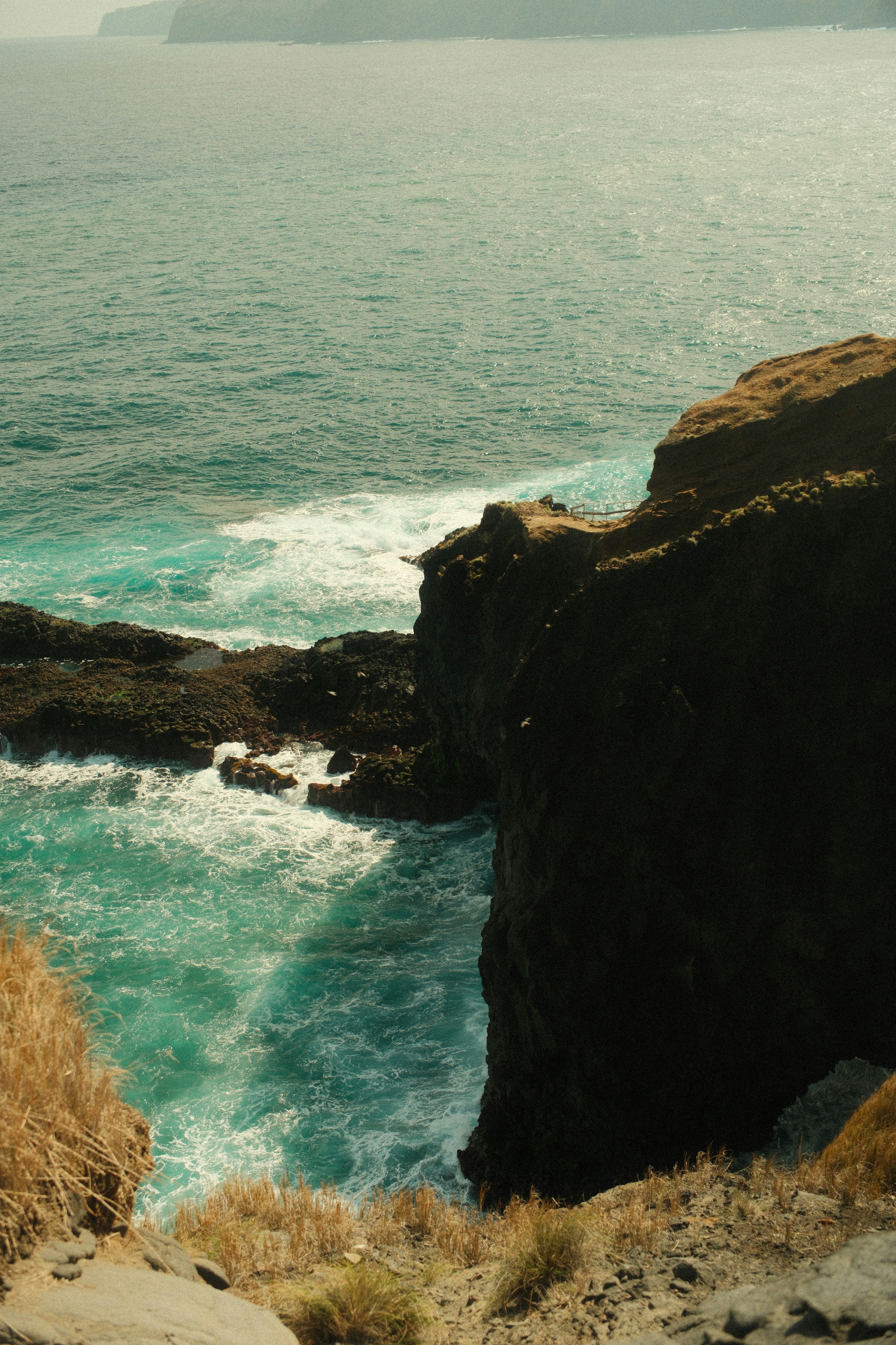 Waves crash against rugged cliffs with distant land visible