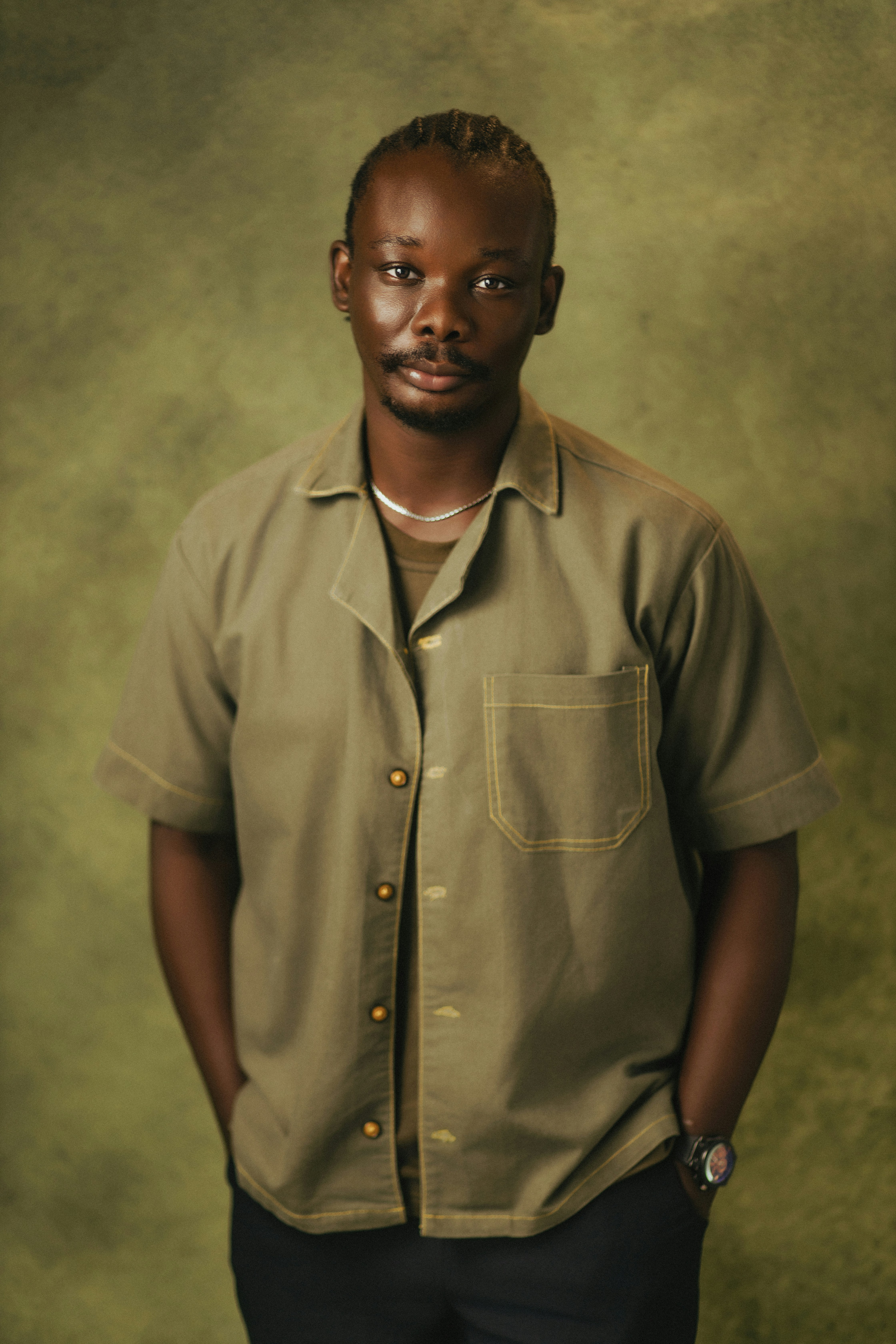A man with braids standing against a green background