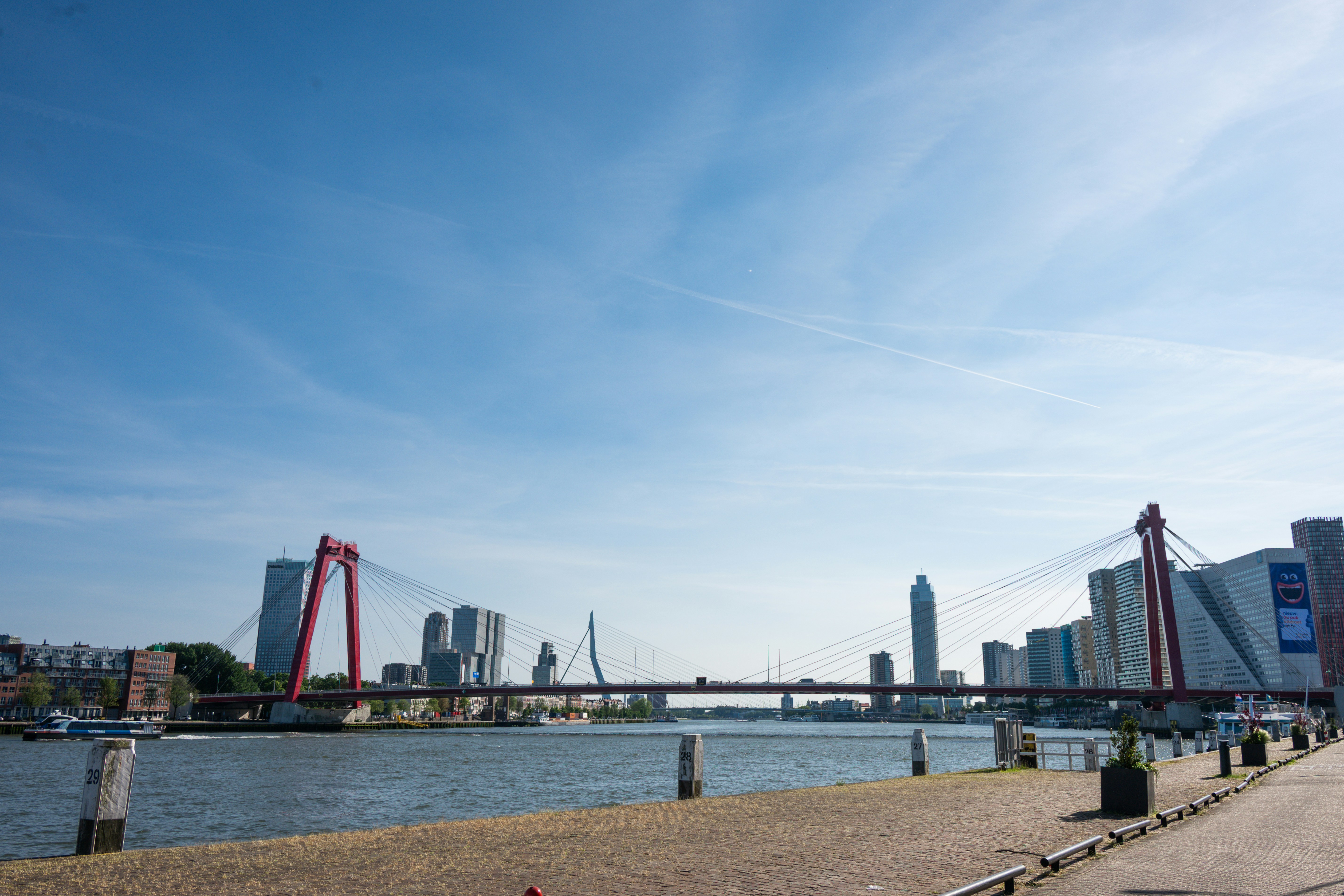 Eine rote Brücke überspannt einen Fluss mit einer Stadtsilhouette.