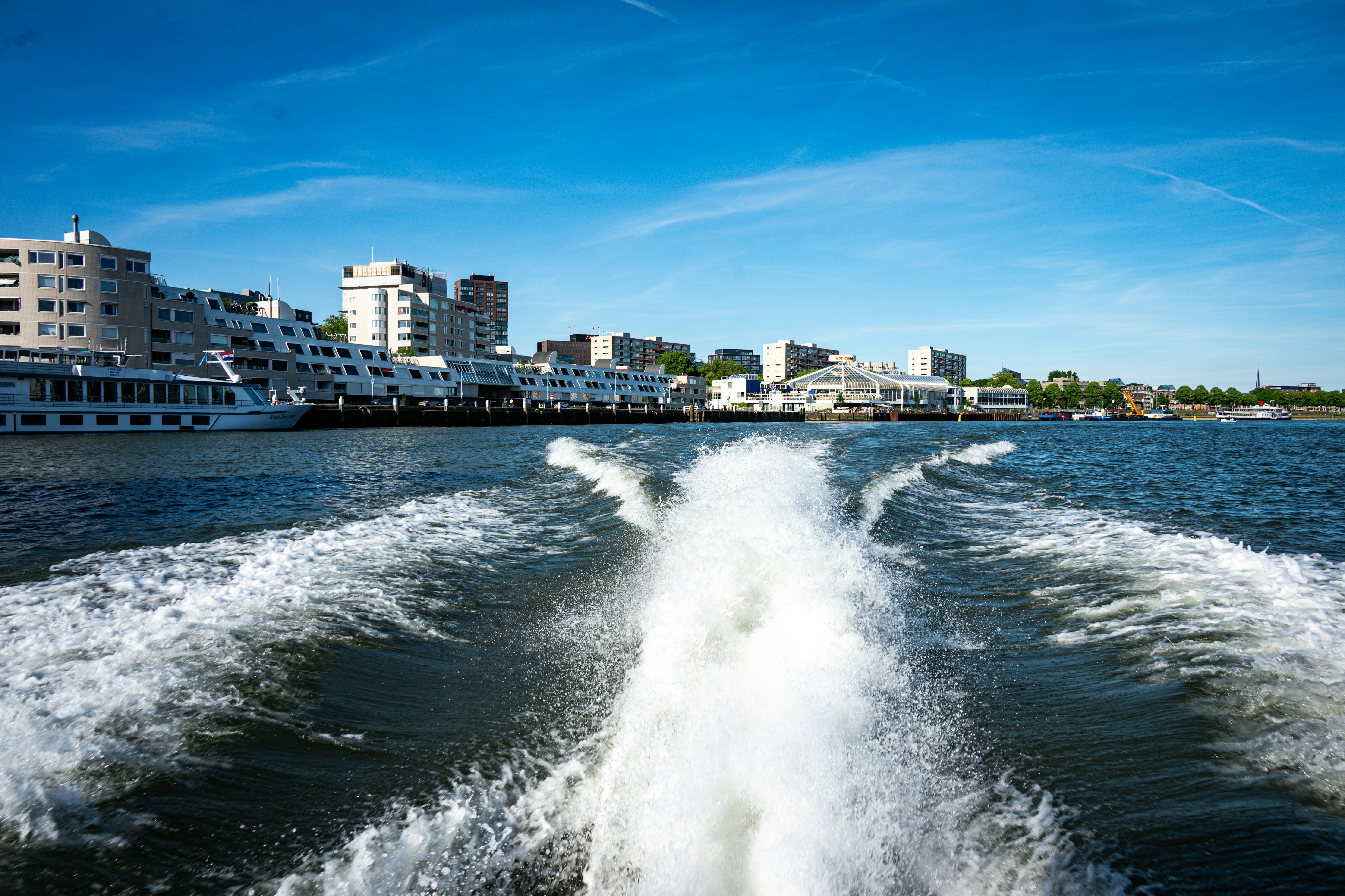 Bootswelle auf Wasser mit Stadtsilhouette unter blauem Himmel.