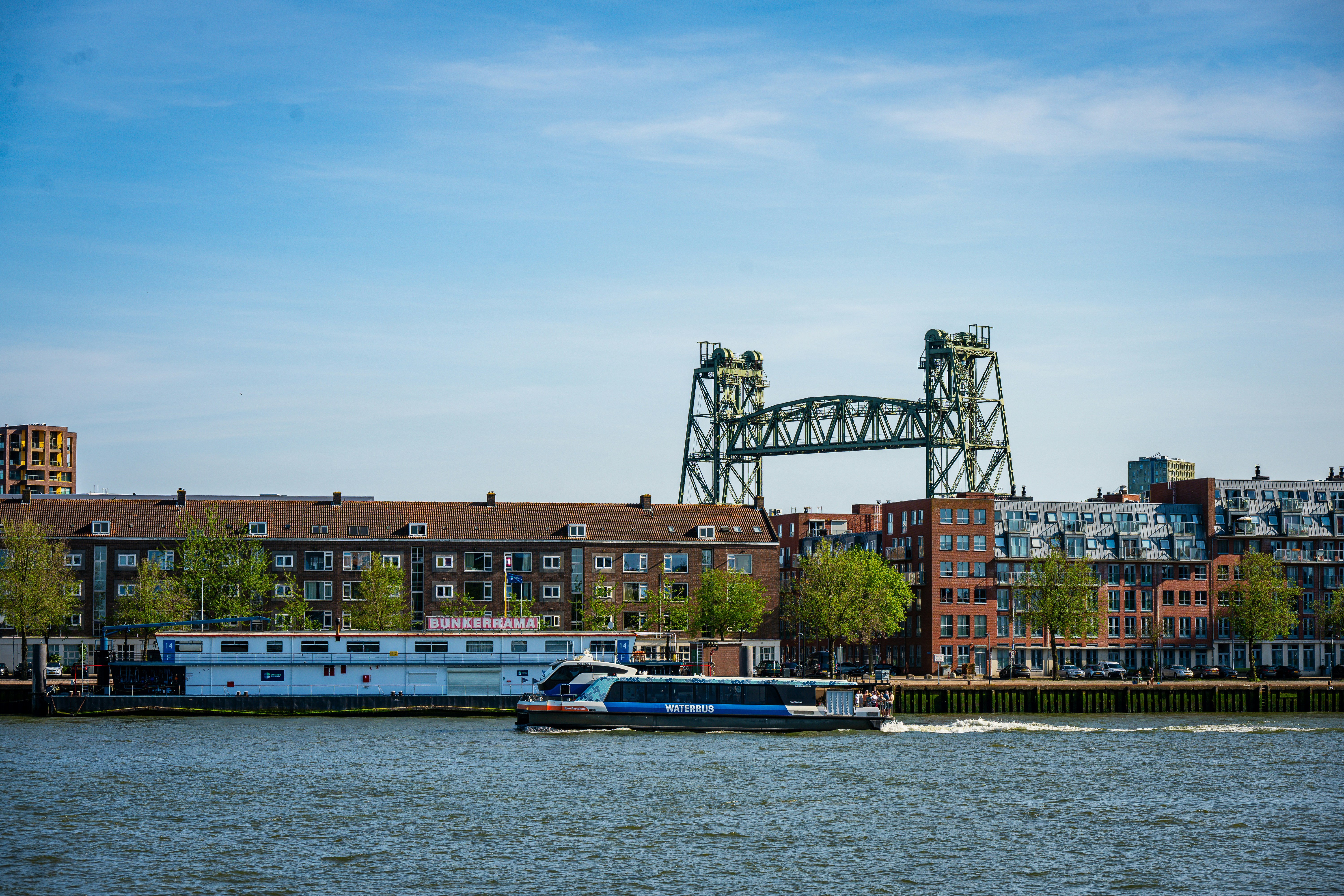 Modernes Boot, das an Stadtgebäuden und einer großen Brücke vorbeifährt.