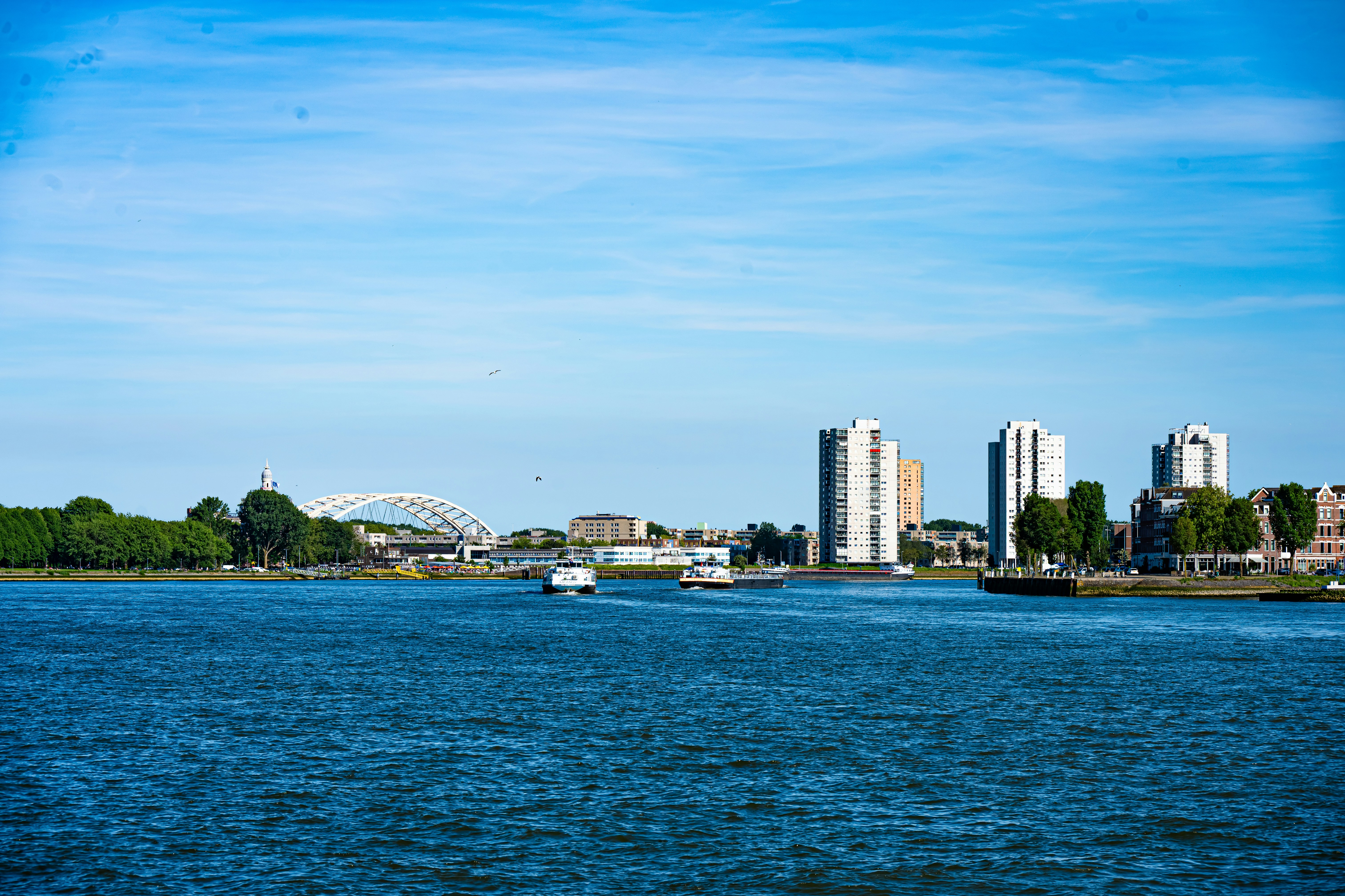 Boote auf blauem Wasser mit Stadtsilhouette und Brücke.