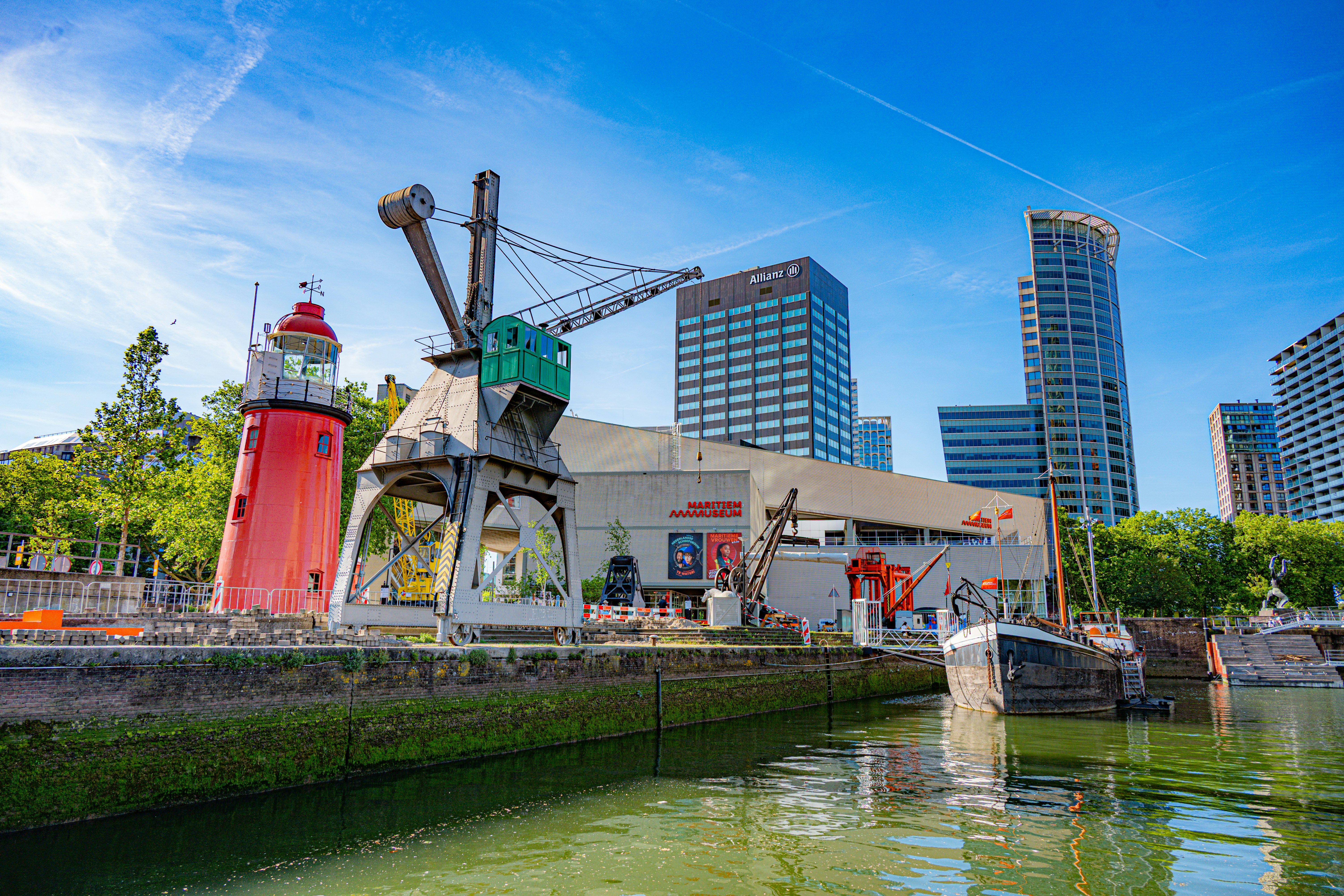 Roter Leuchtturm und Kran am Wasser mit Stadtsilhouette.