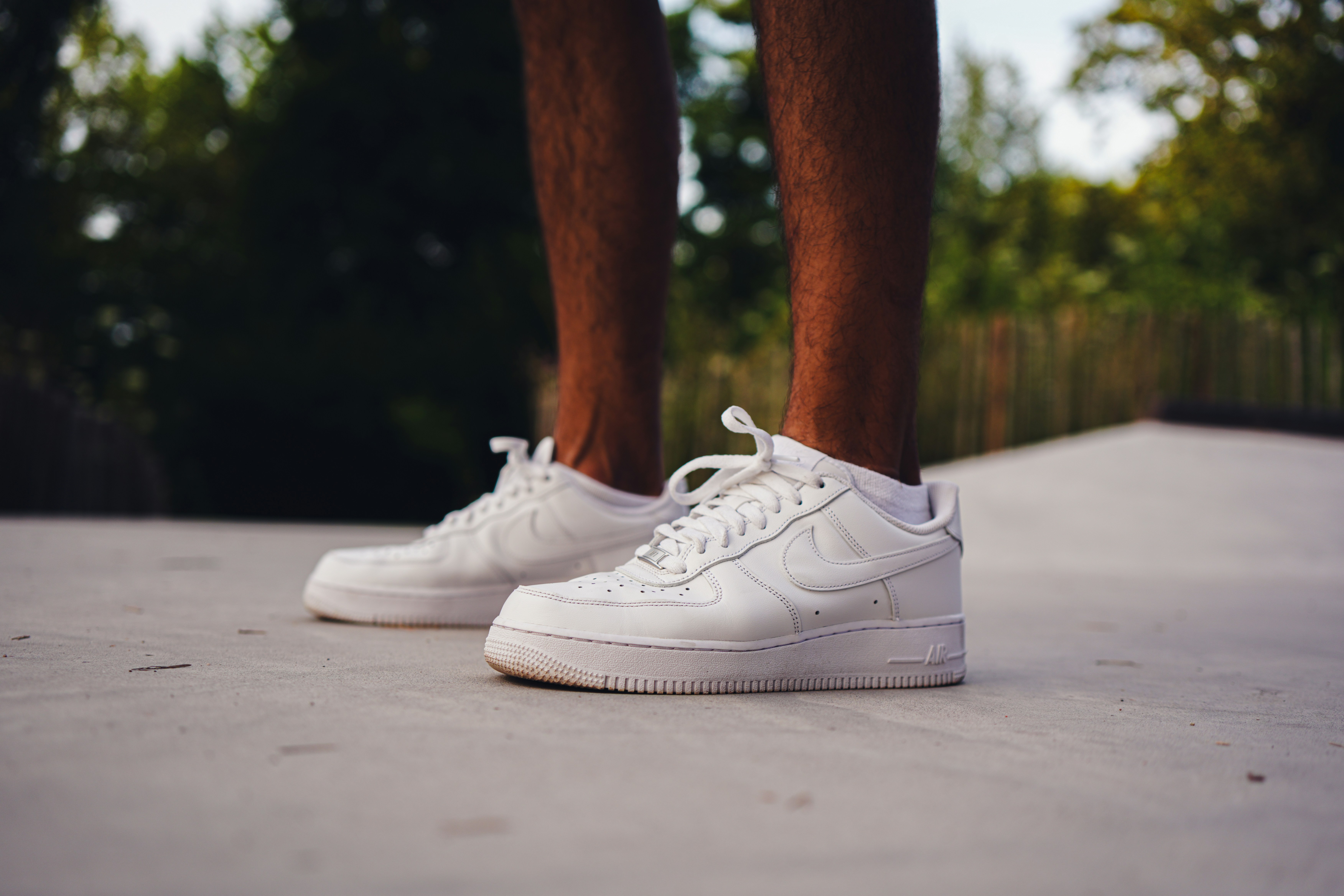 Feet in white sneakers on a concrete surface outdoors.