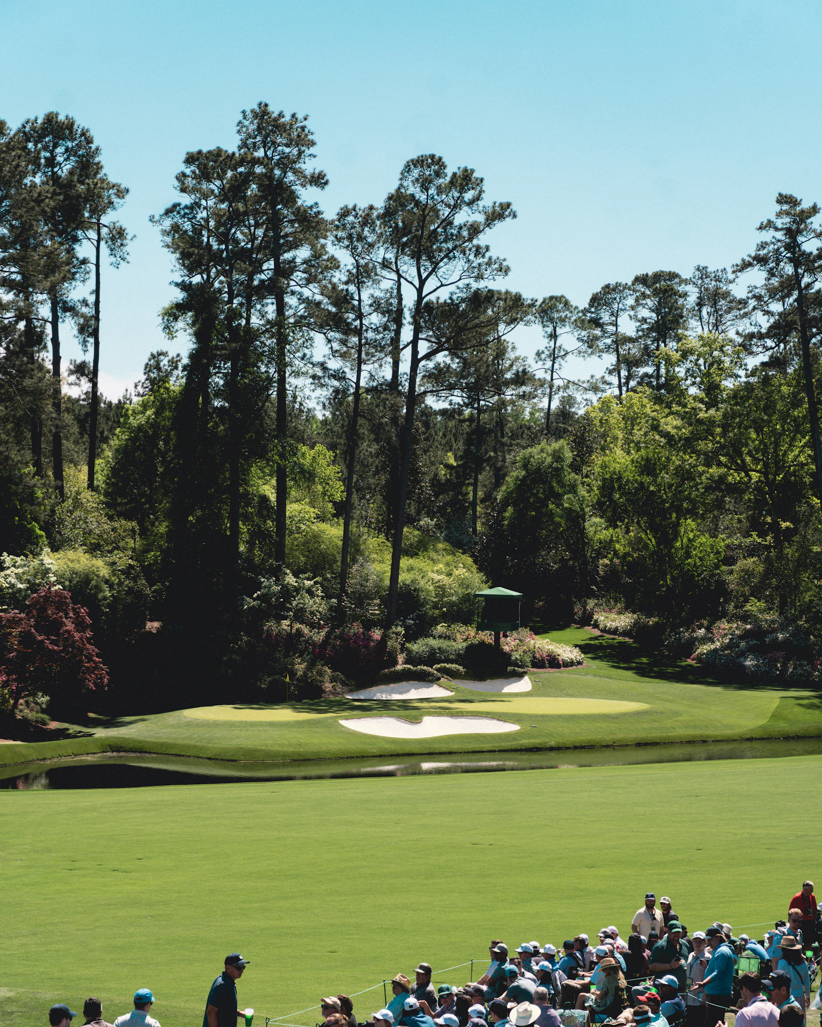 Spectators beside a tree-lined fairway with bunkers at a golf tournament