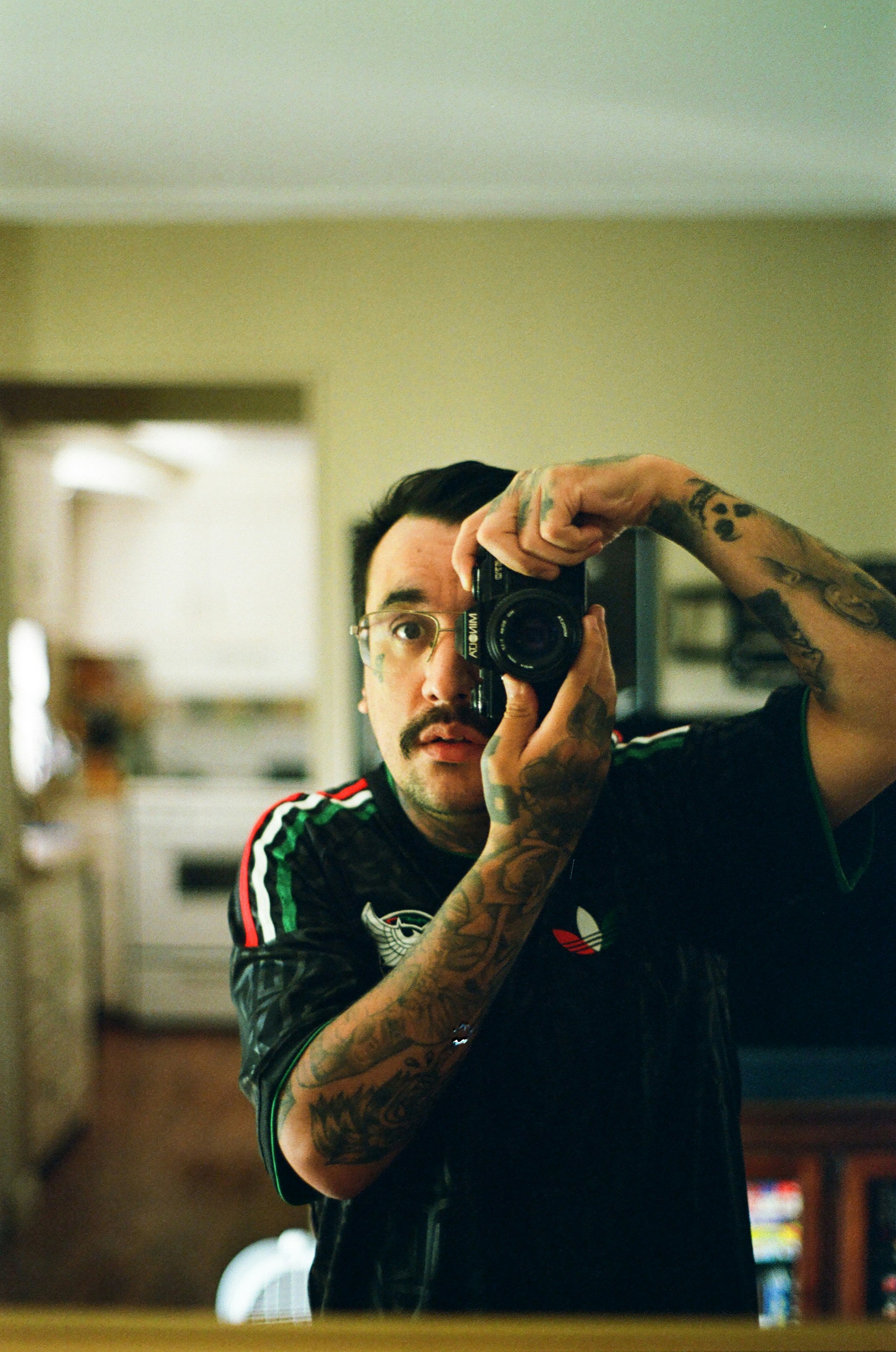 A tattooed man taking a mirror selfie with a camera