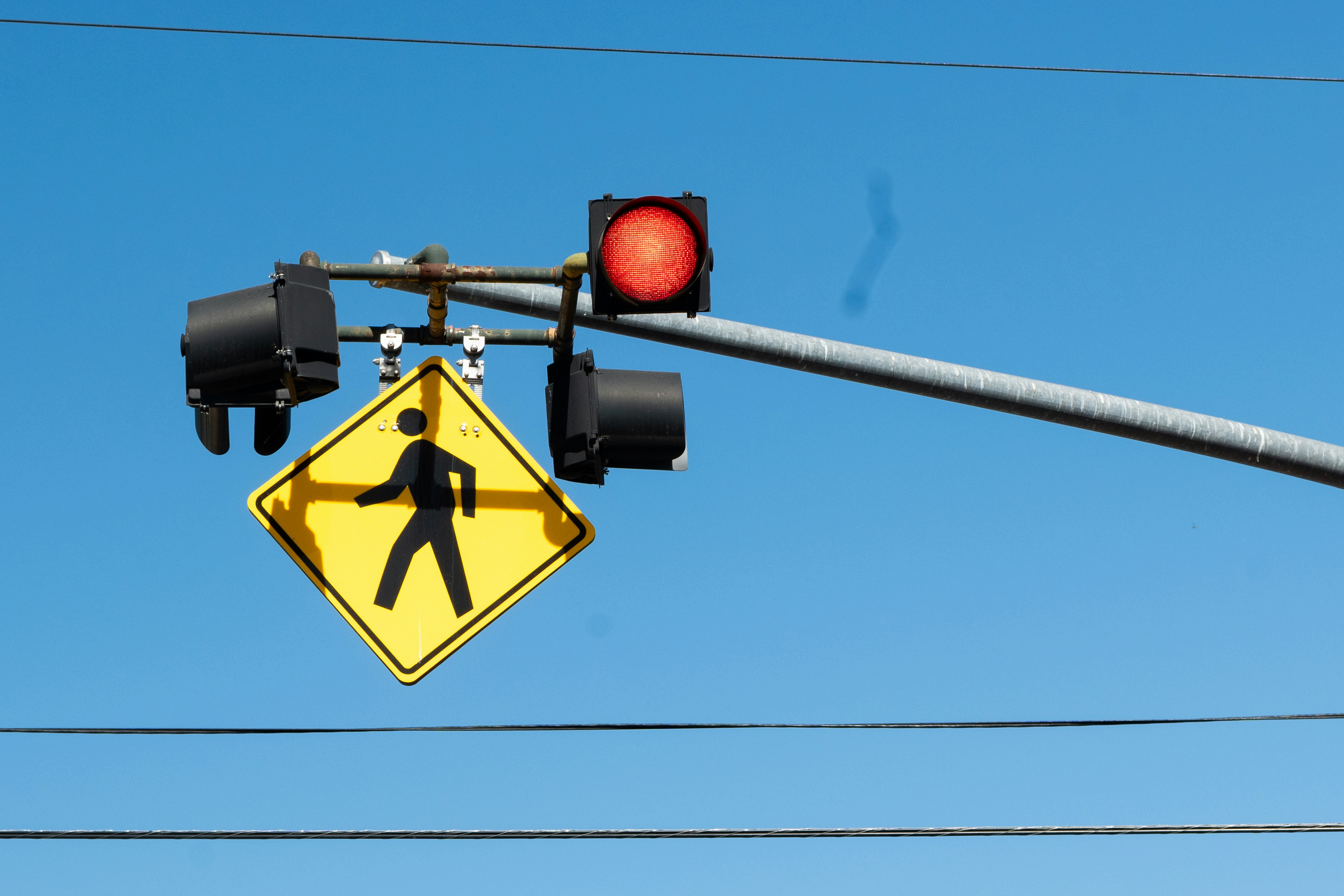 A red traffic light with a yellow pedestrian crossing sign