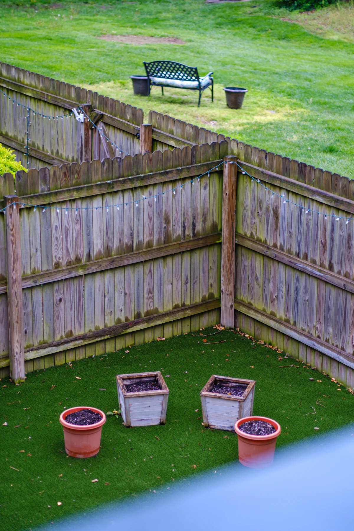 A small enclosed backyard with dated timber fencing, artificial turf and empty planters