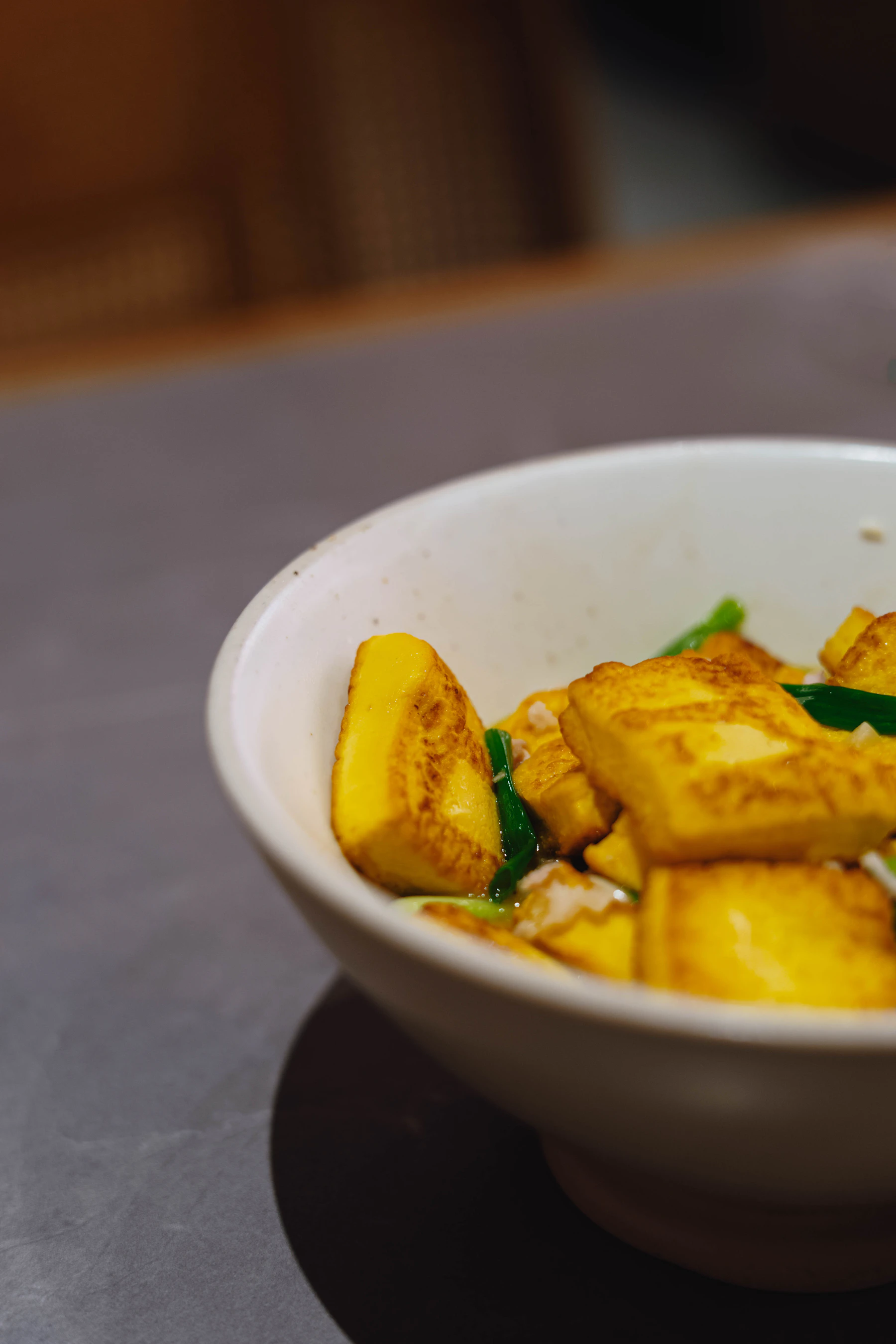 Golden pan-fried tofu with scallions in a white bowl
