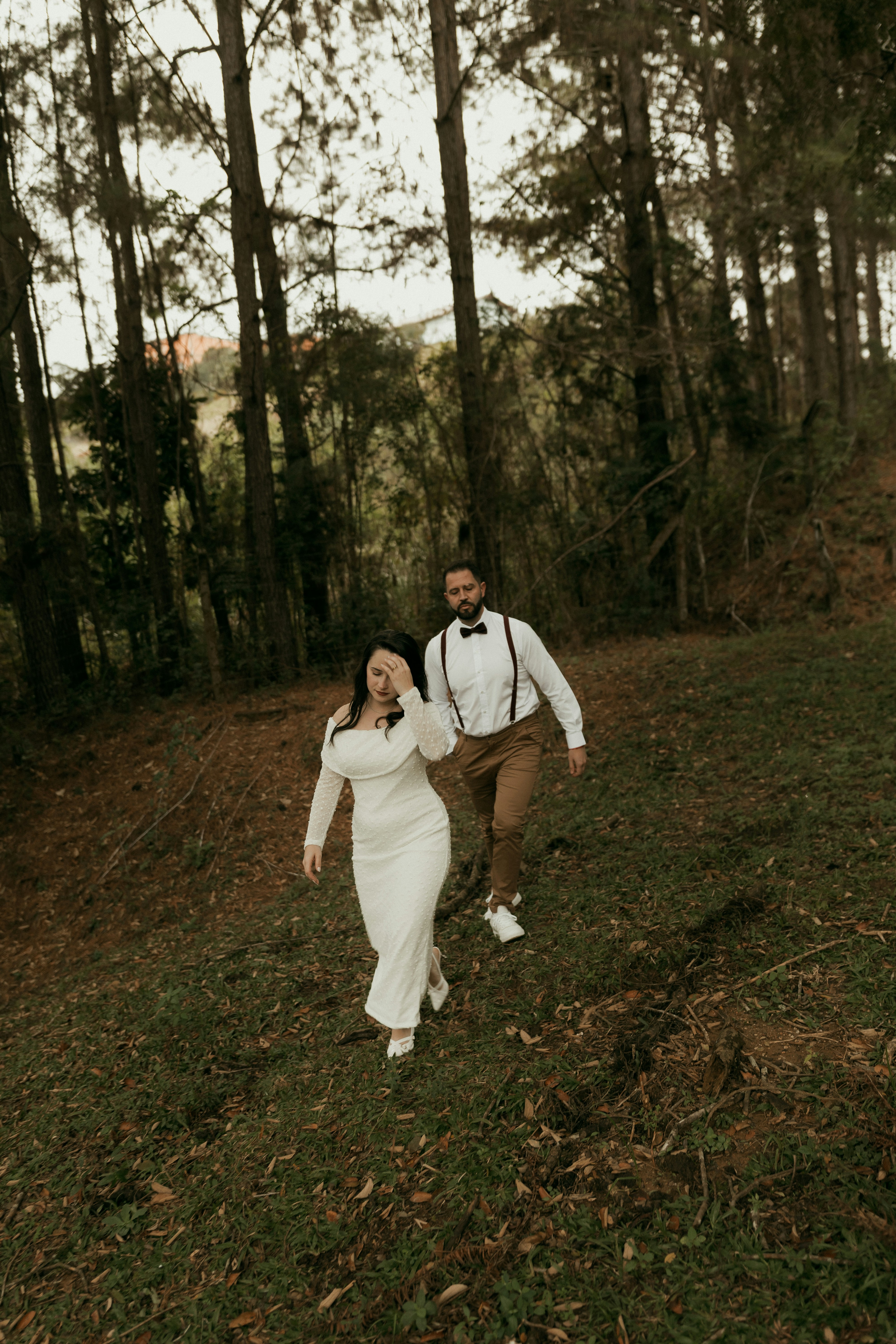 Elegant couple walking uphill through a serene forest.