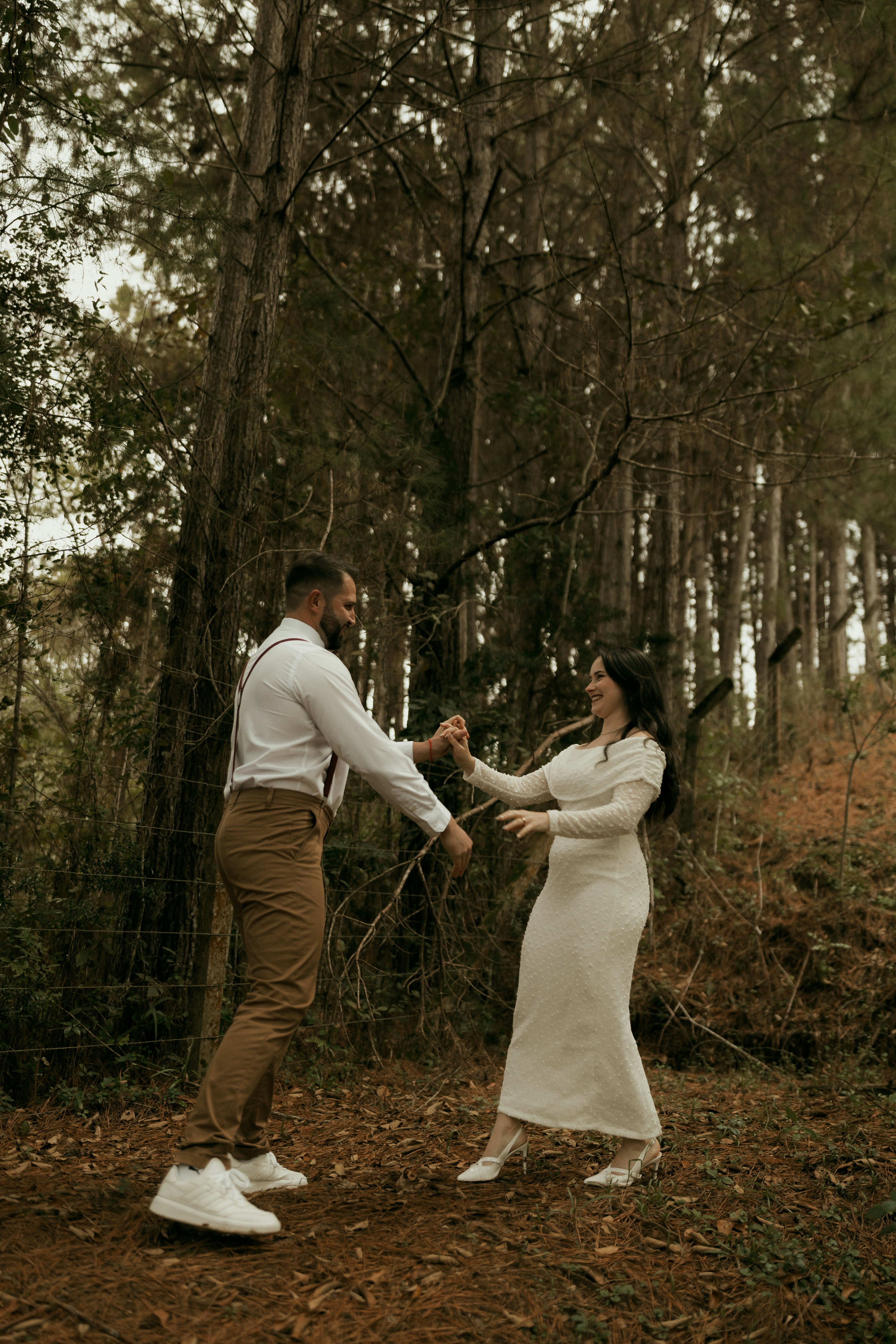 Happy couple dancing hand-in-hand among tall trees.