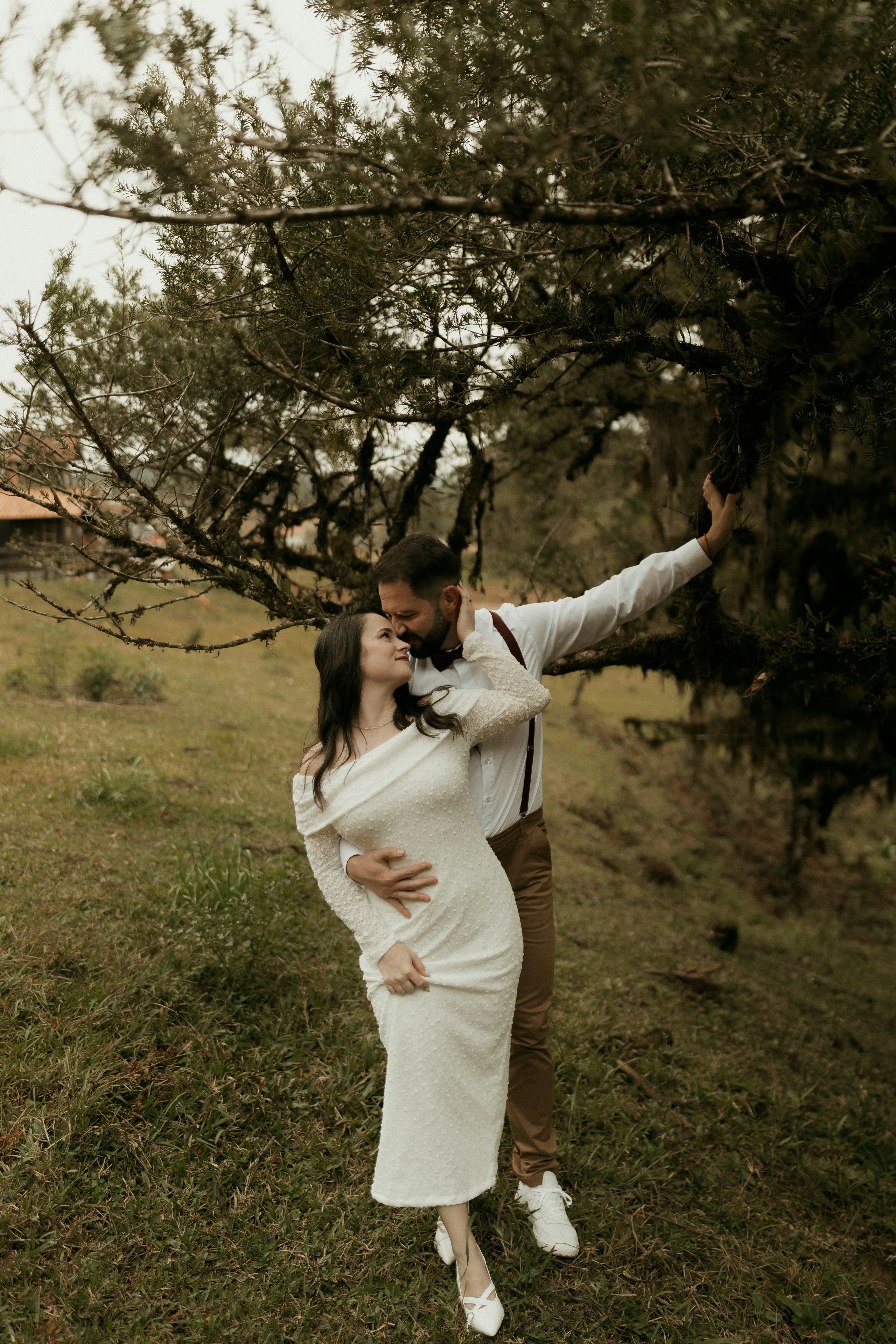 A couple embraces under a tree in a natural setting.