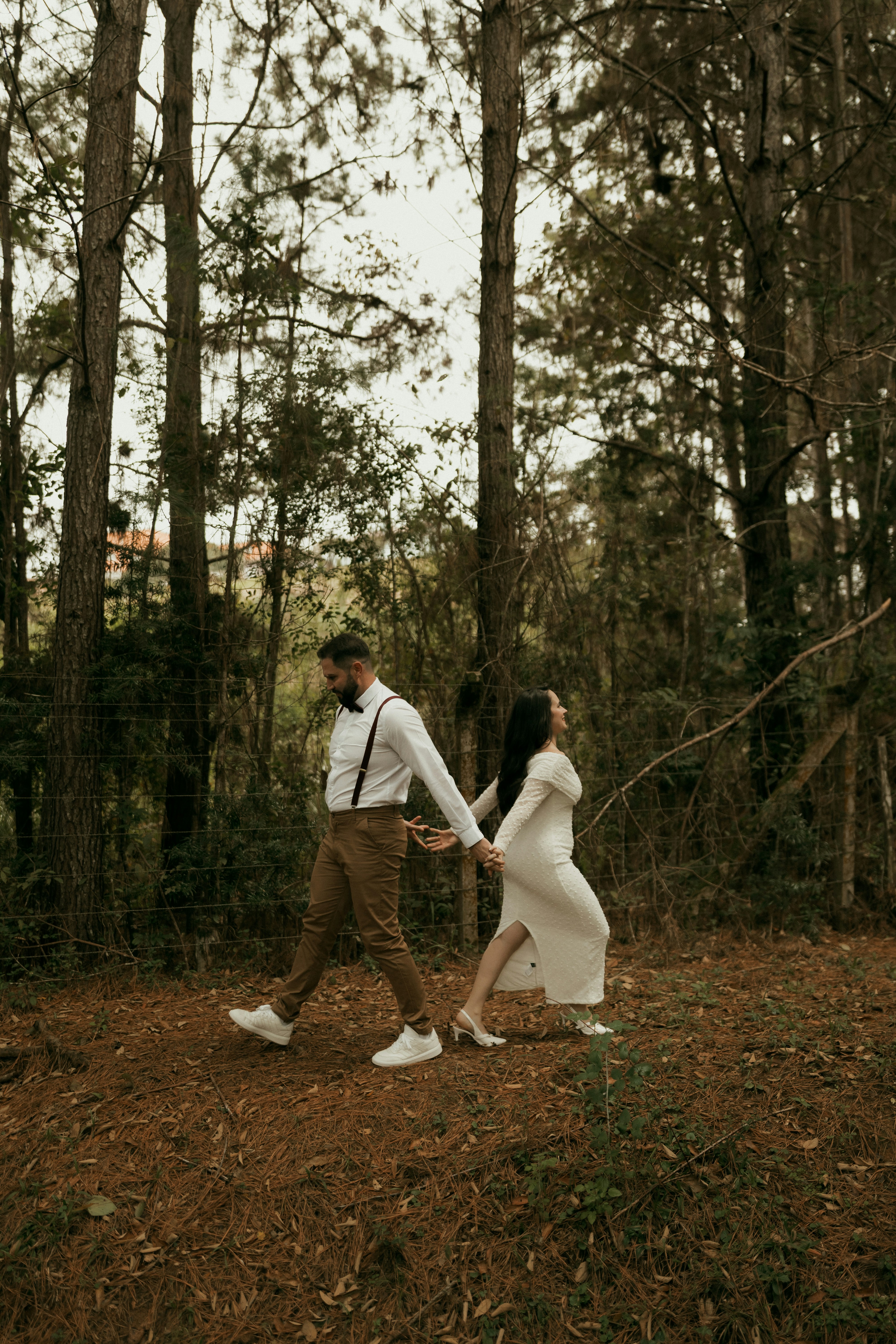 Couple holding hands walking back-to-back in a forest.