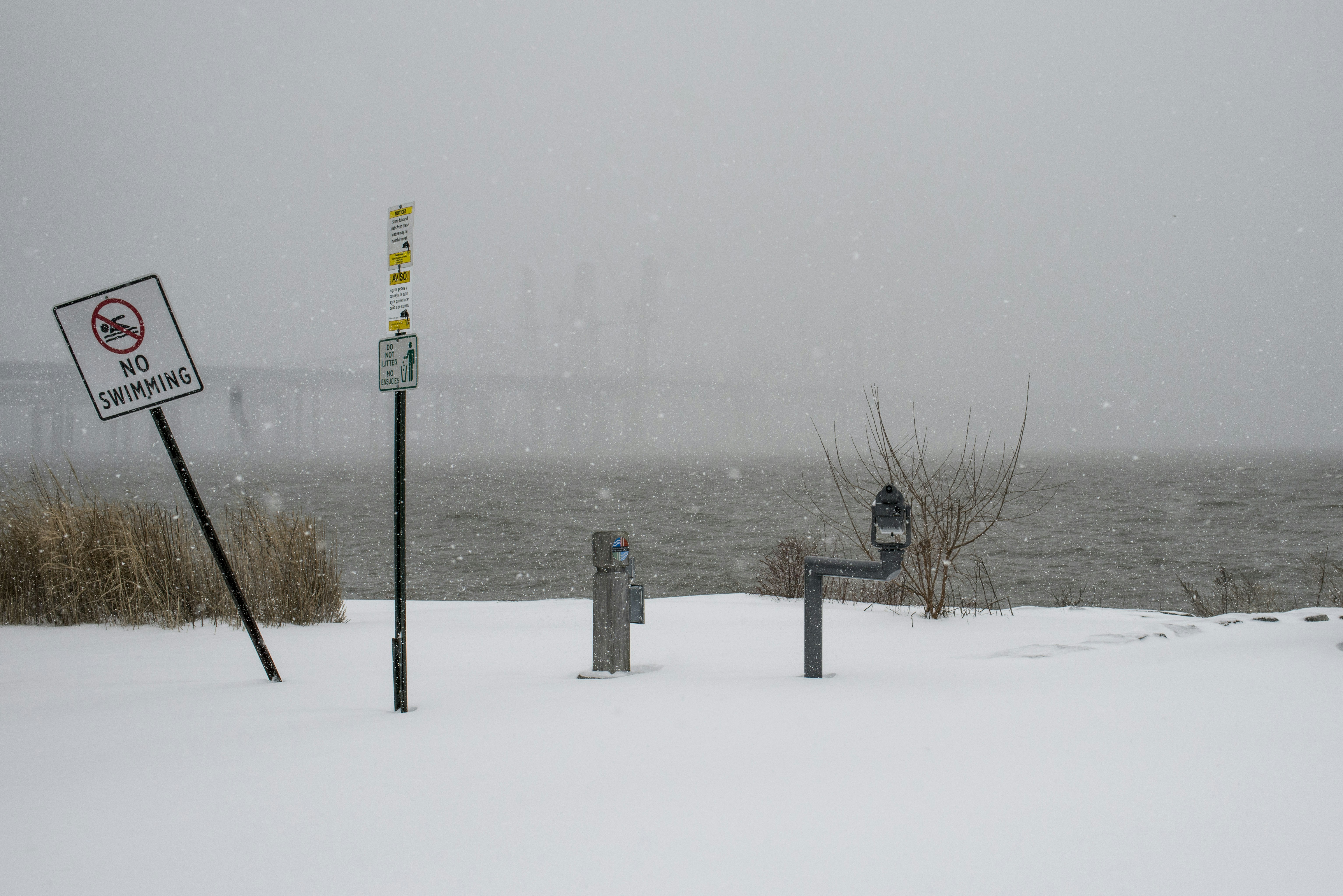 A snowy waterfront with signs and a grey, hazy sky