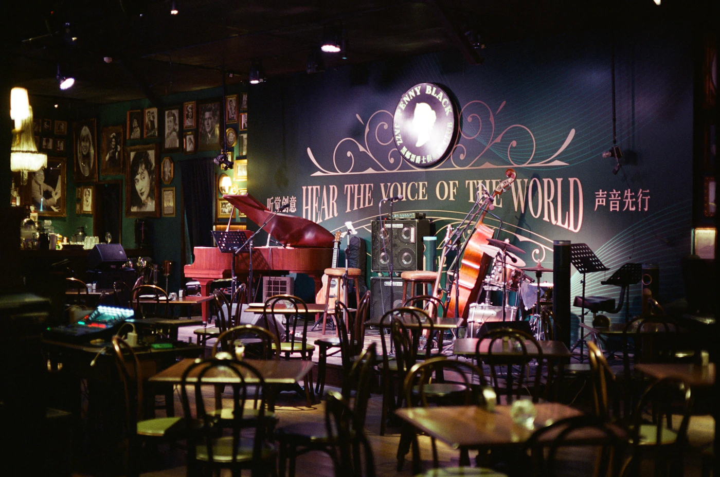 A dark music club with a piano on stage and empty tables