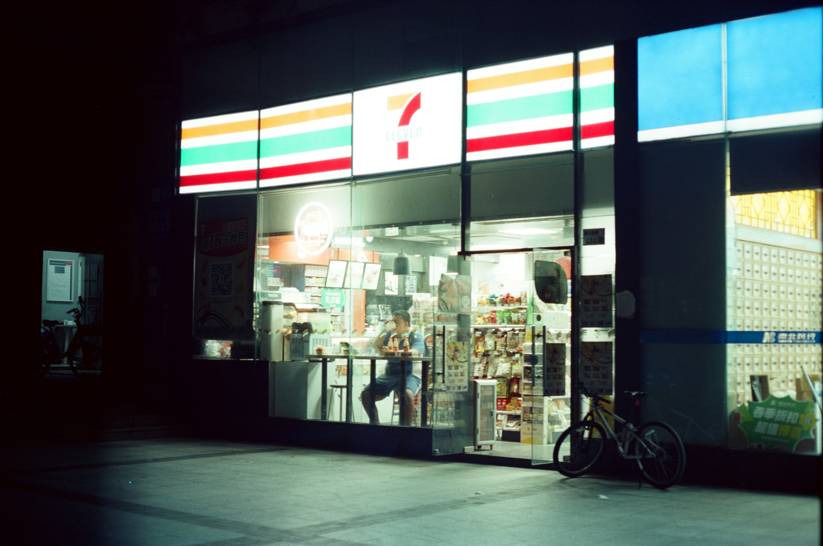 A 7-eleven convenience store illuminated at night with a bicycle.