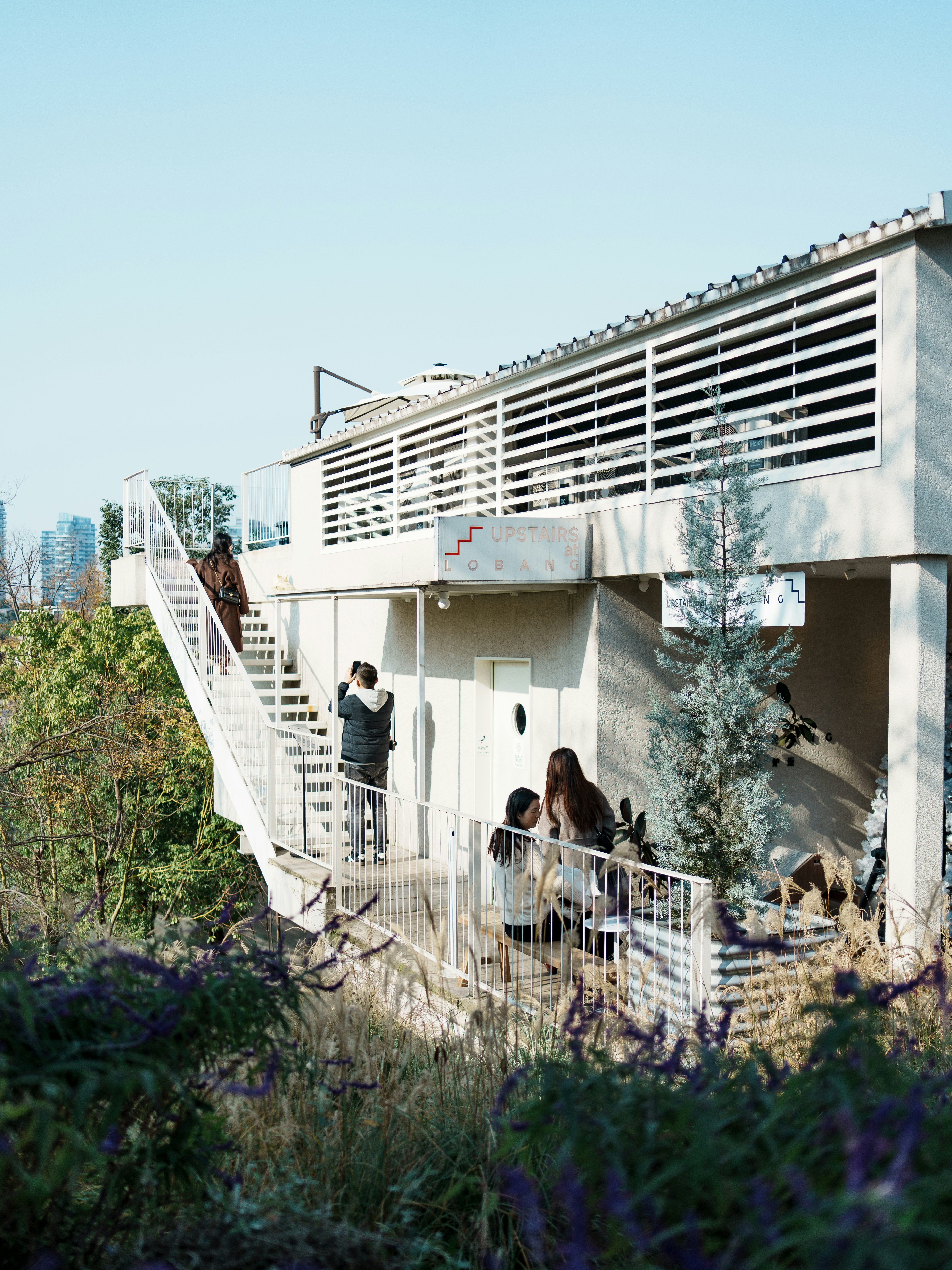 People ascend white stairs of a contemporary building in nature.