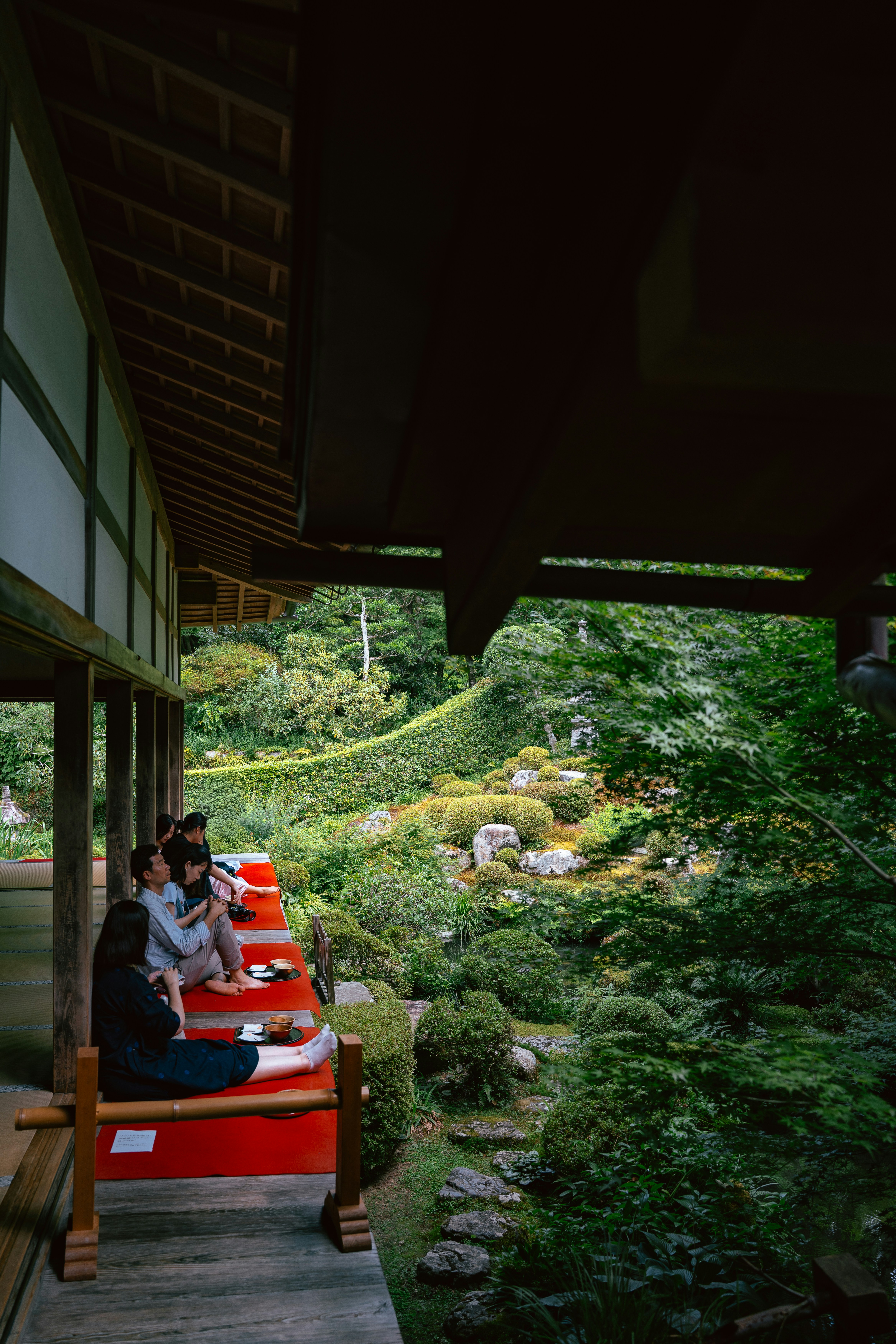 Orang-orang duduk di beranda yang menghadap taman Jepang yang rimbun