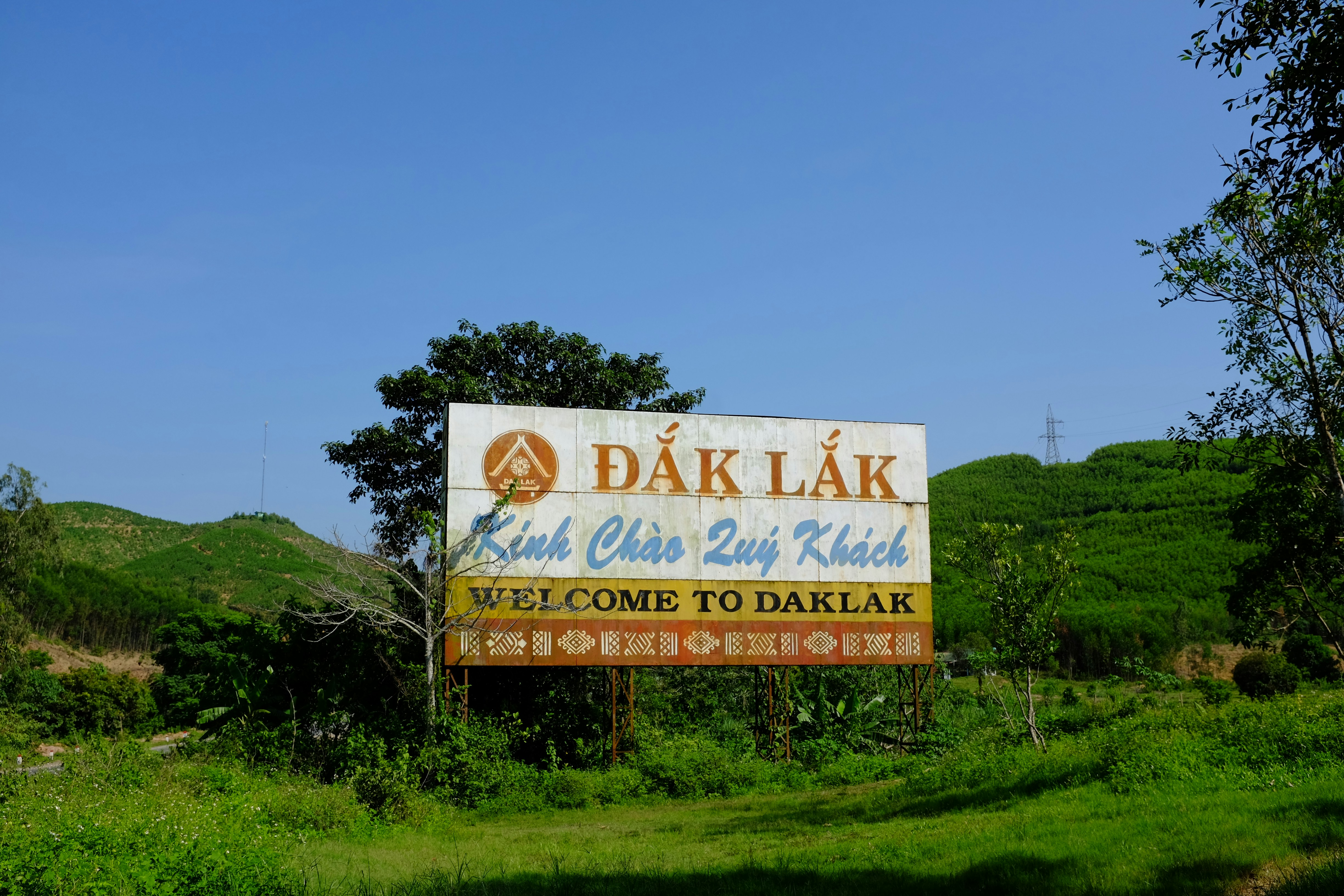 A "welcome to daklak" sign stands amidst green hills