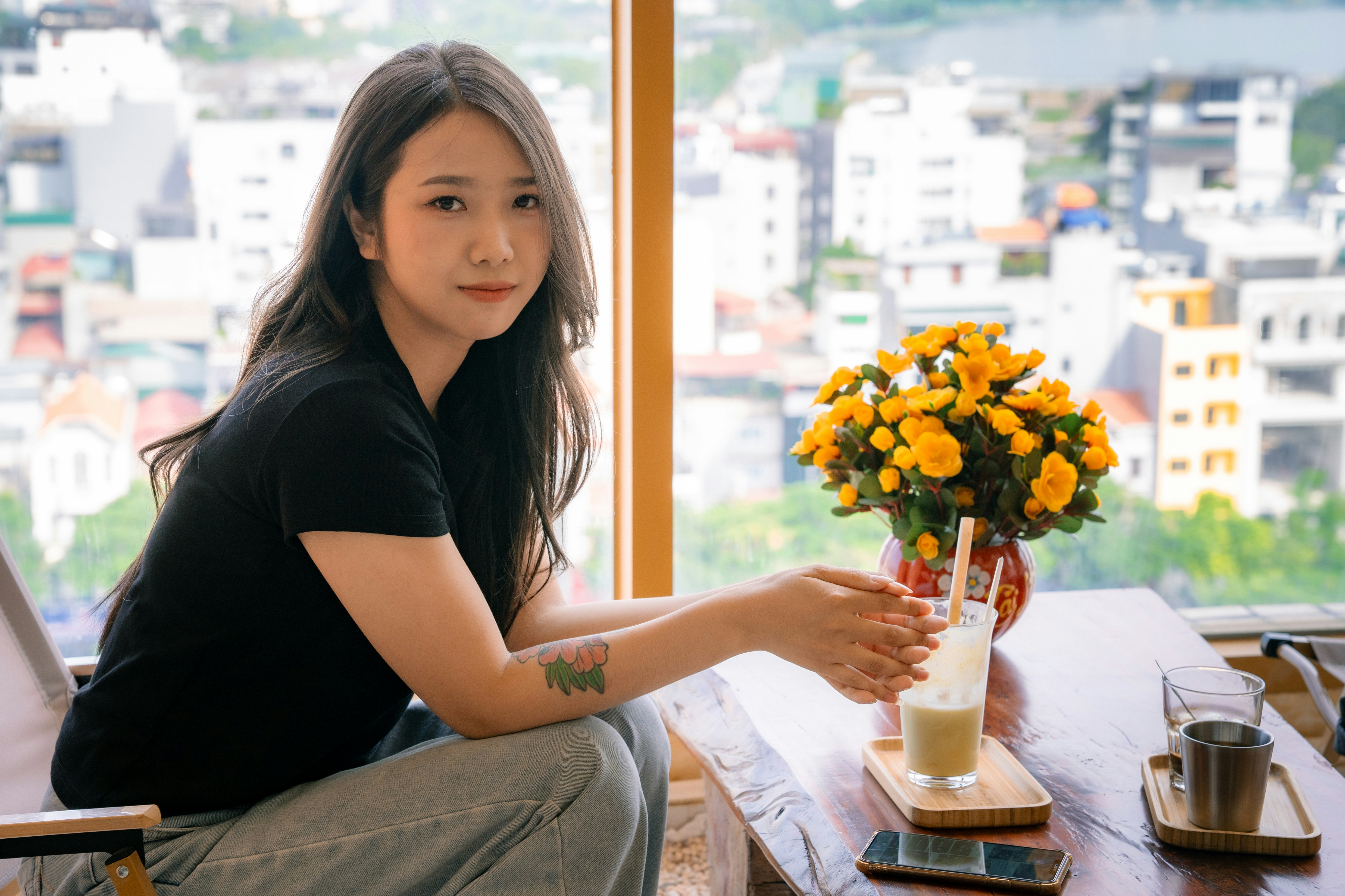 Young woman sitting by window with cityscape and yellow flowers