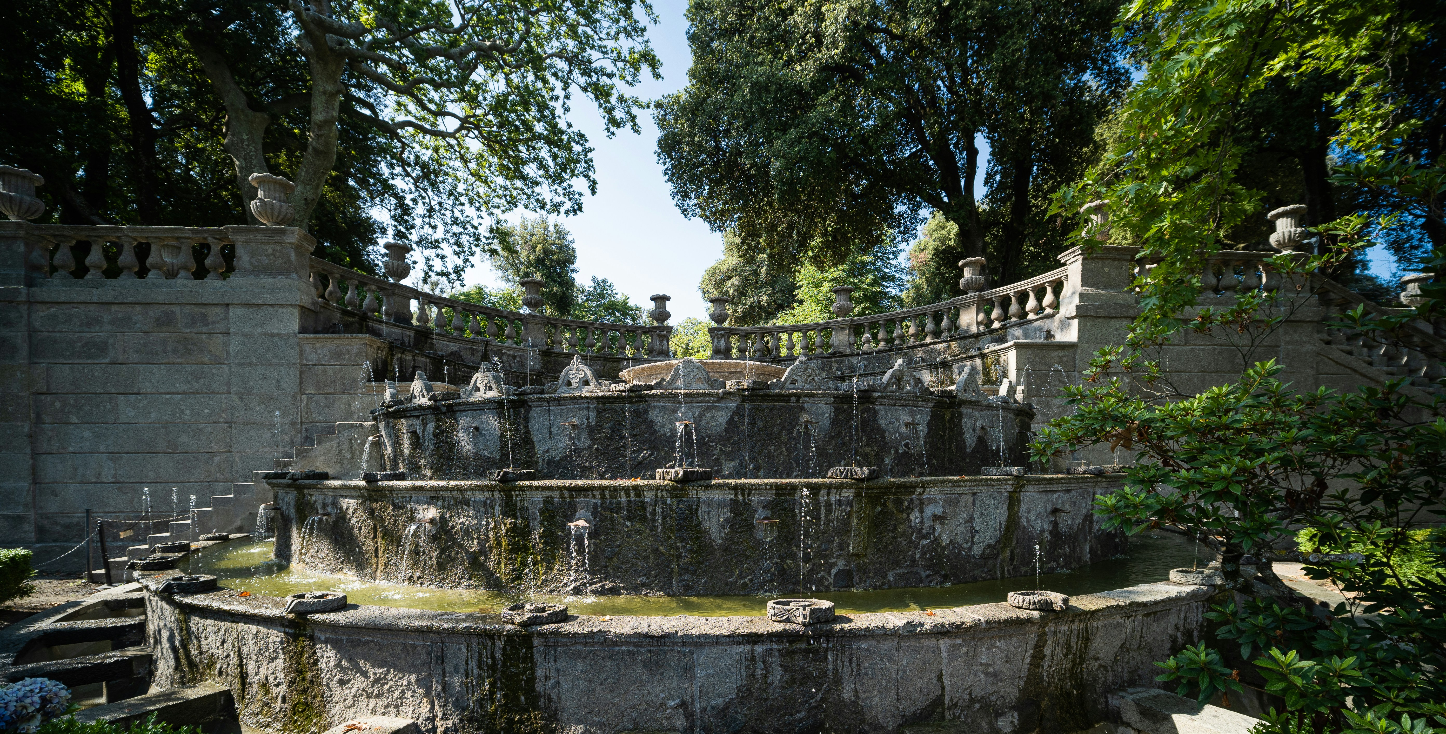 A multi-tiered stone fountain flowing in a lush green garden.