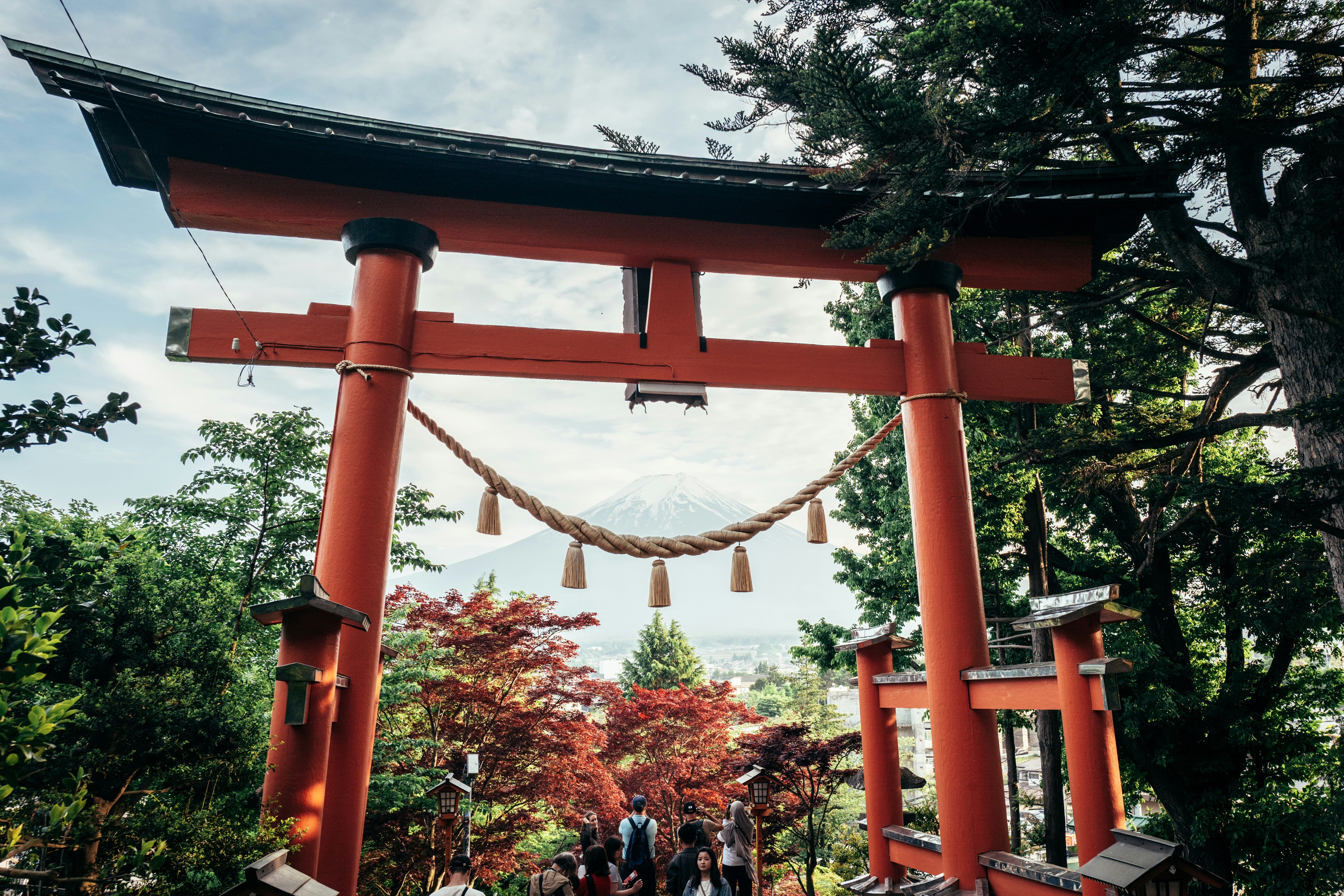 A red torii gate frames mount fuji and lush trees