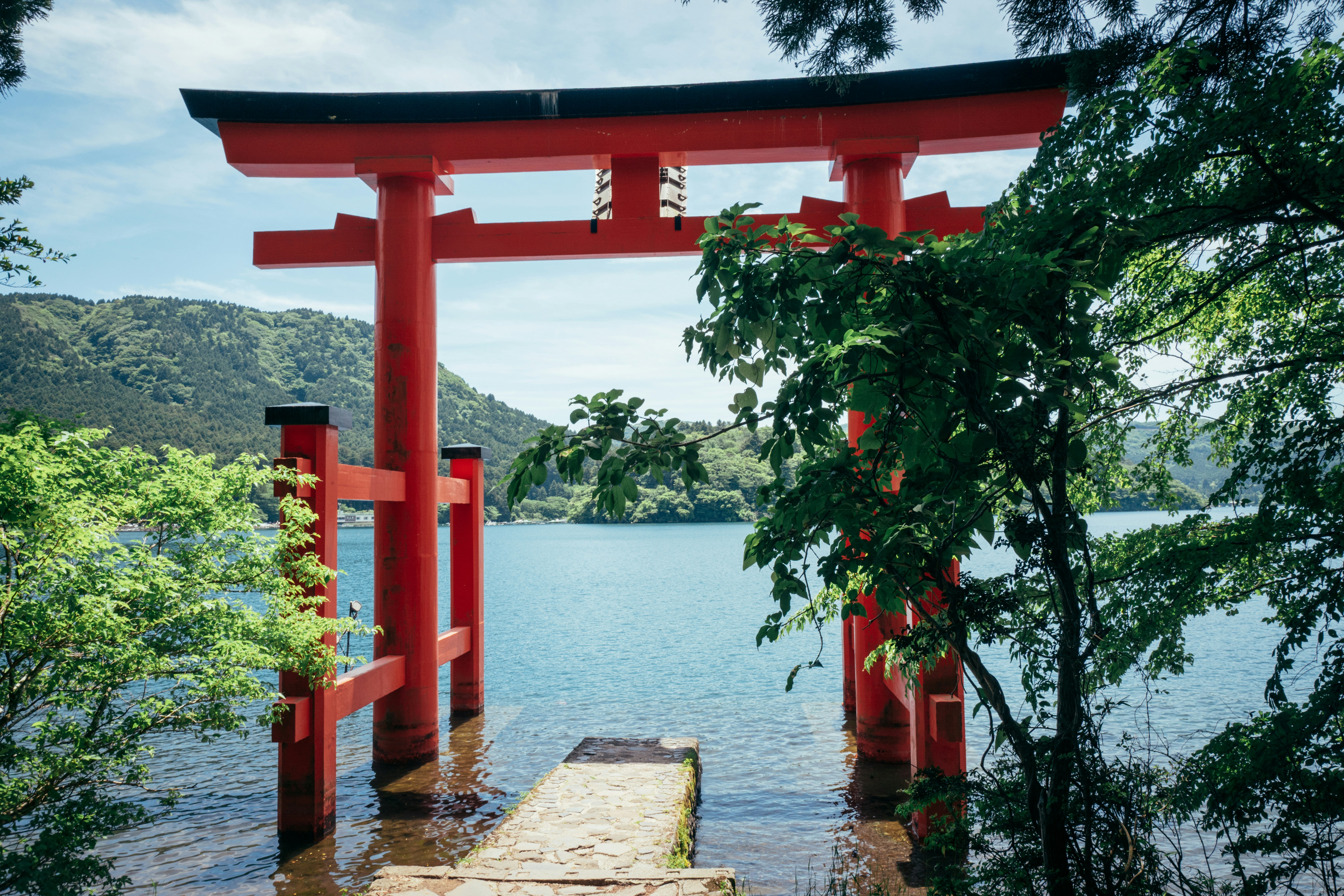 A red torii gate stands in a lake with mountains