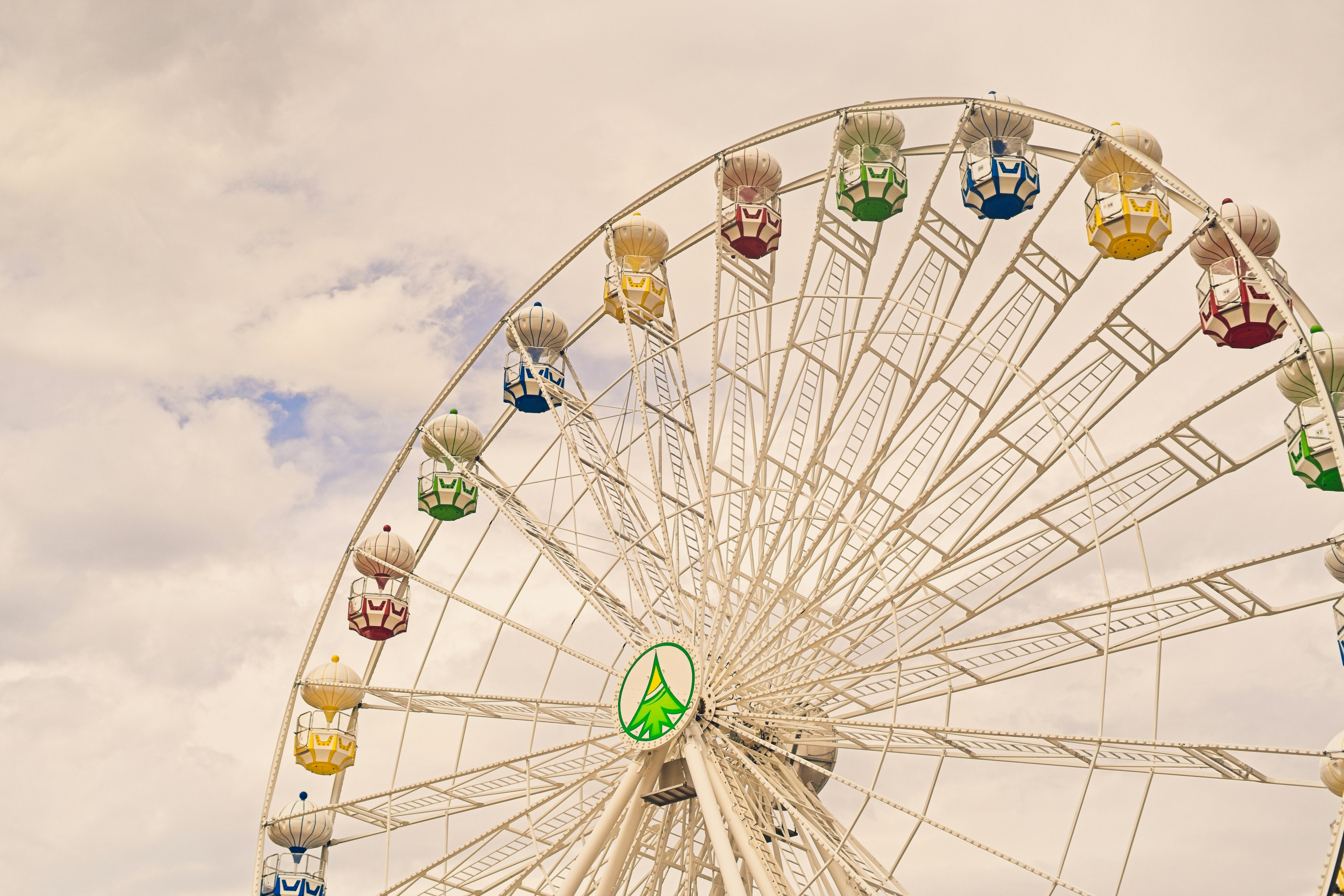 Colorful gondolas on a white ferris wheel against cloudy sky.