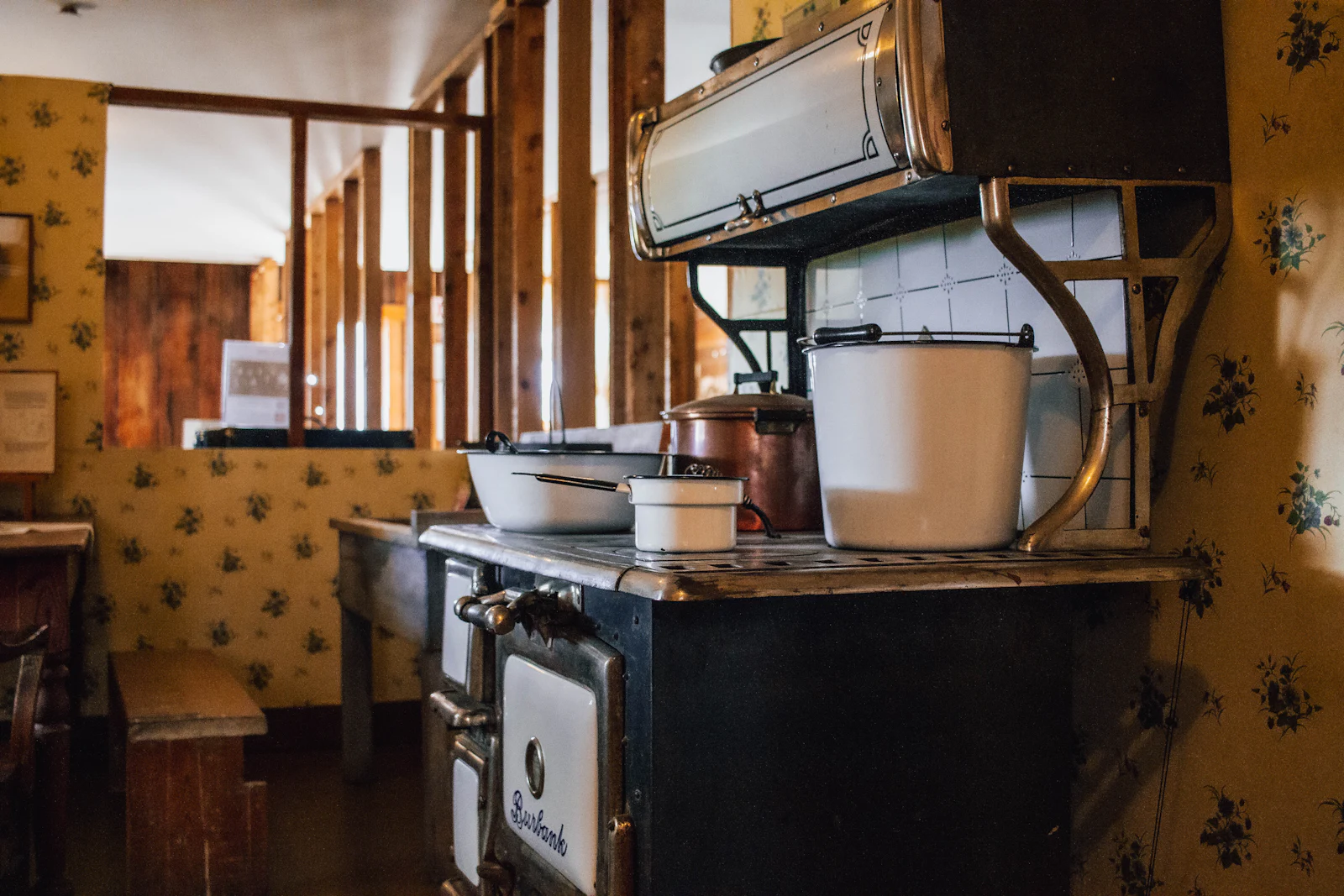 An old kitchen with a large cast iron stove and patterned wallpaper.