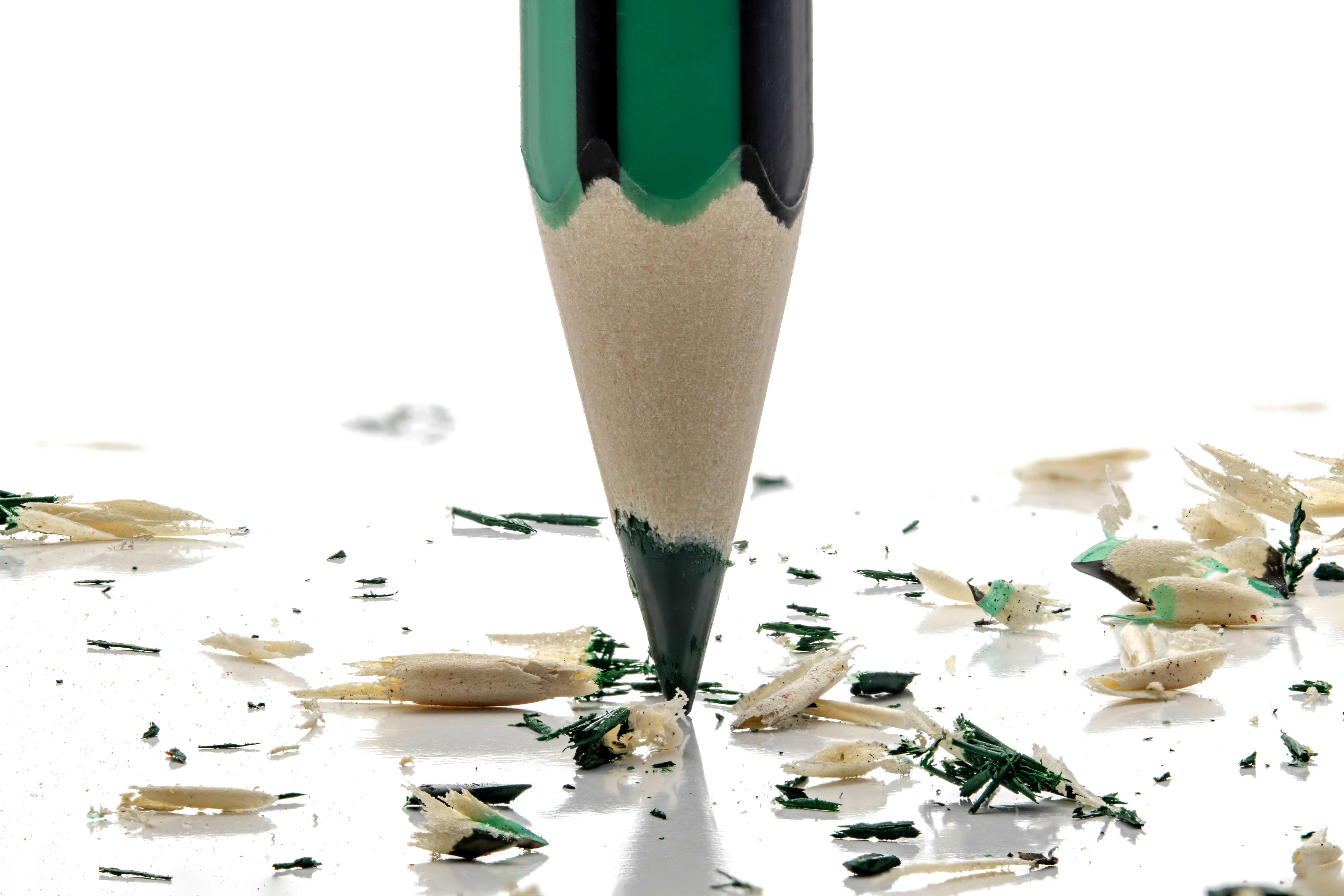 A green pencil point down with wood shavings on white