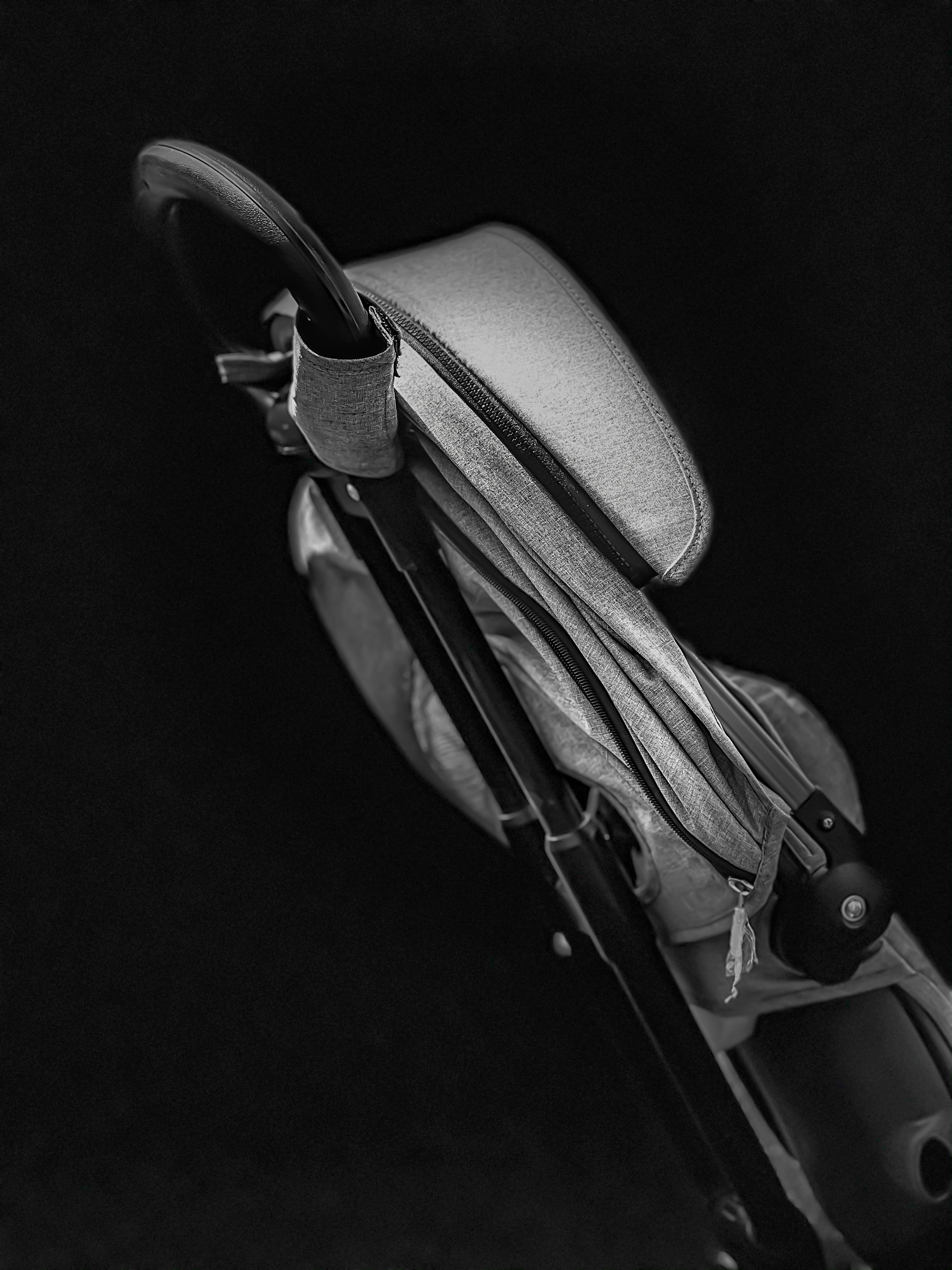 Black-and-white close-up of a folded stroller, its grey fabric seat and frame tucked together